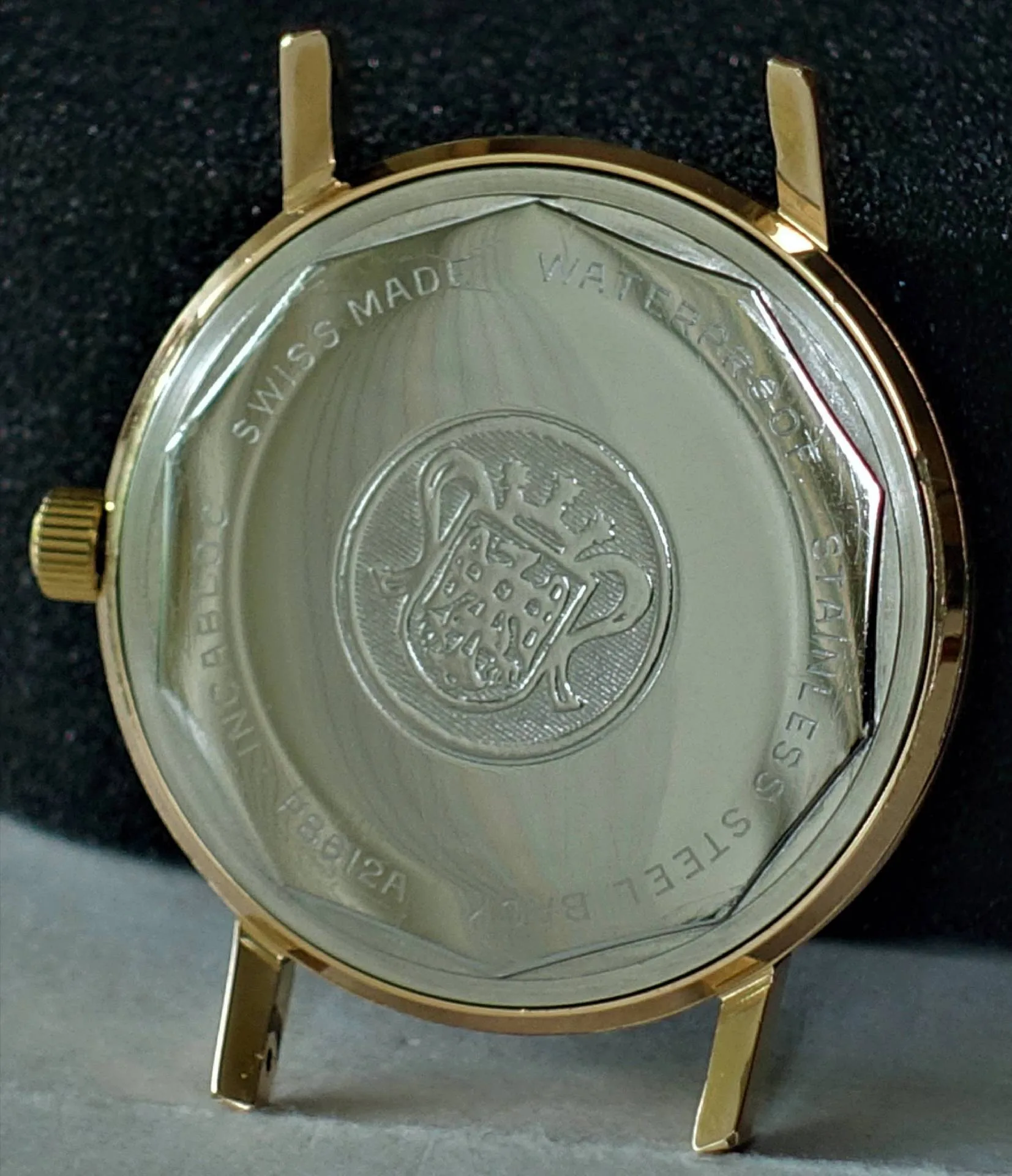 Goldfarbenes Uhrgehäuse mit silberfarbener Rückseite und Gravur eines Wappens.