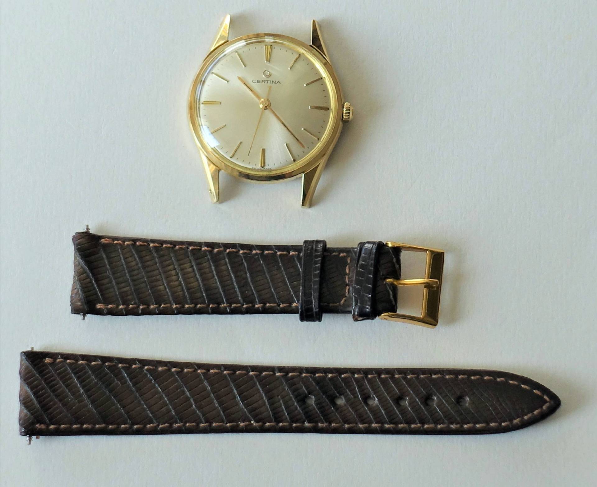 Zerlegte goldfarbene Certina Armbanduhr mit hellem Zifferblatt und braunem Armband aus Leder.