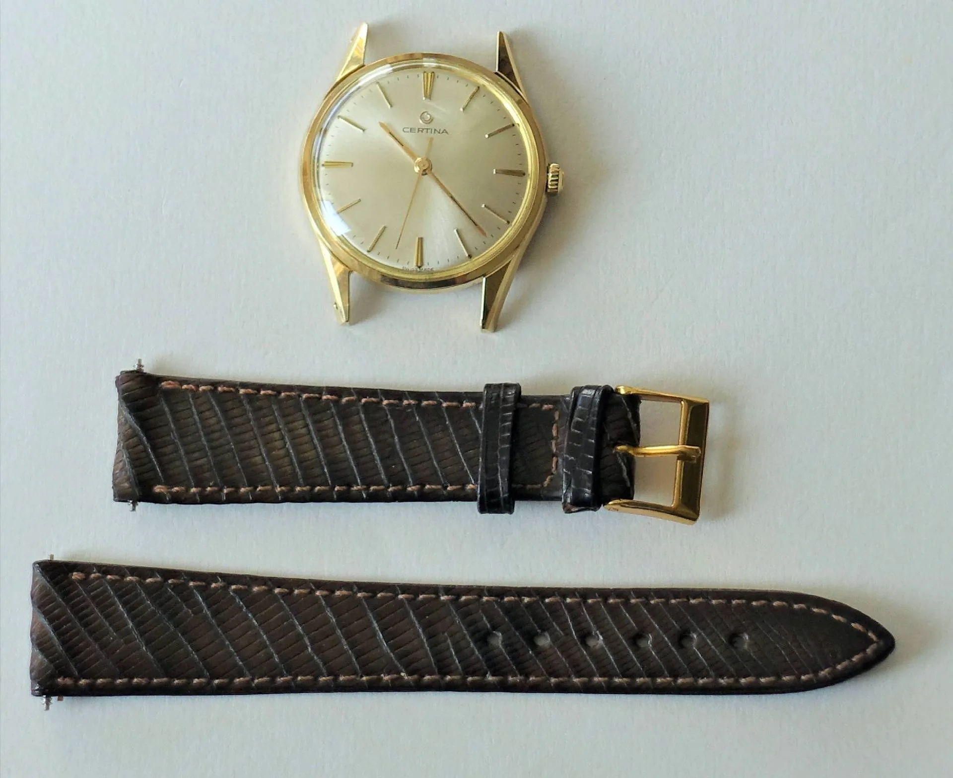 Zerlegte goldfarbene Certina Armbanduhr mit hellem Zifferblatt und braunem Armband aus Leder.