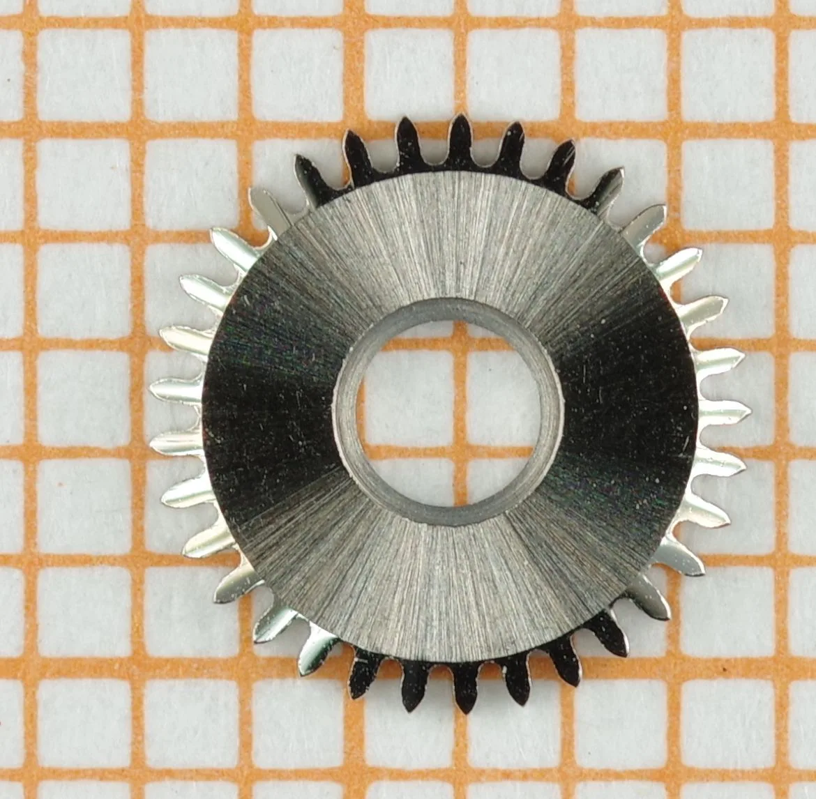 Rundes Zahnrad aus Metall für Uhrwerke, mit feinen Zähnen und zentraler Öffnung.