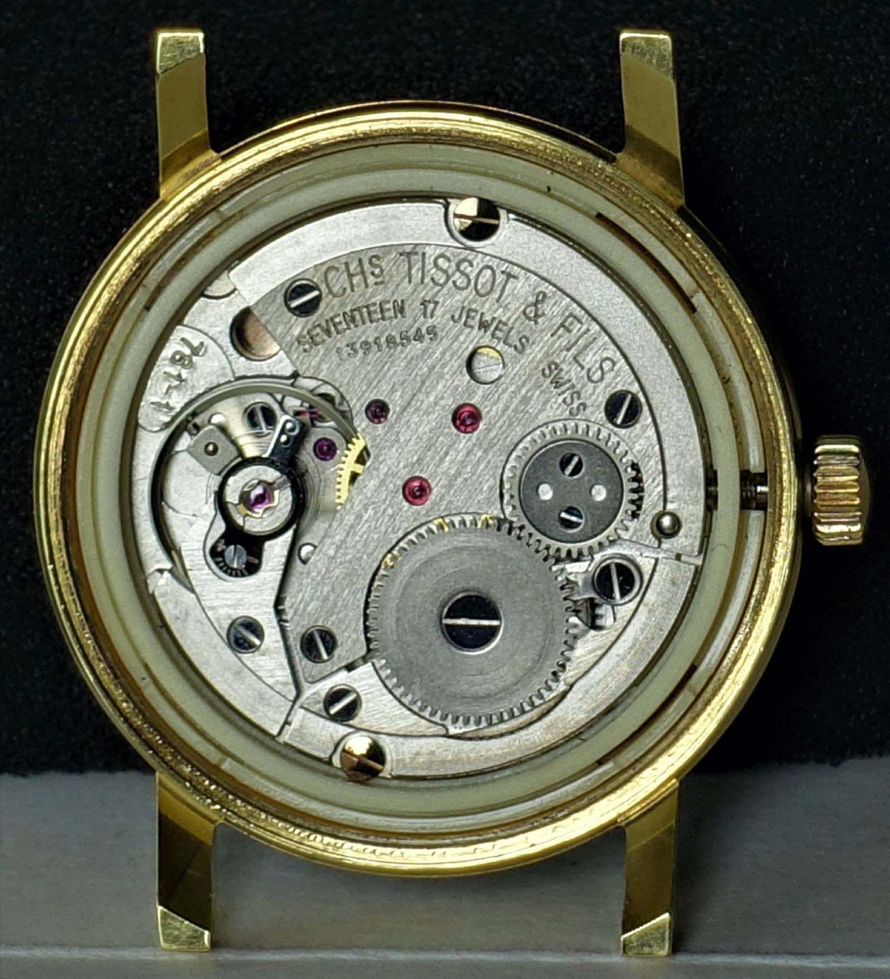 Mechanisches Uhrwerk in einem goldfarbenen Uhrengehäuse mit sichtbaren Zahnrädern und Schrauben.