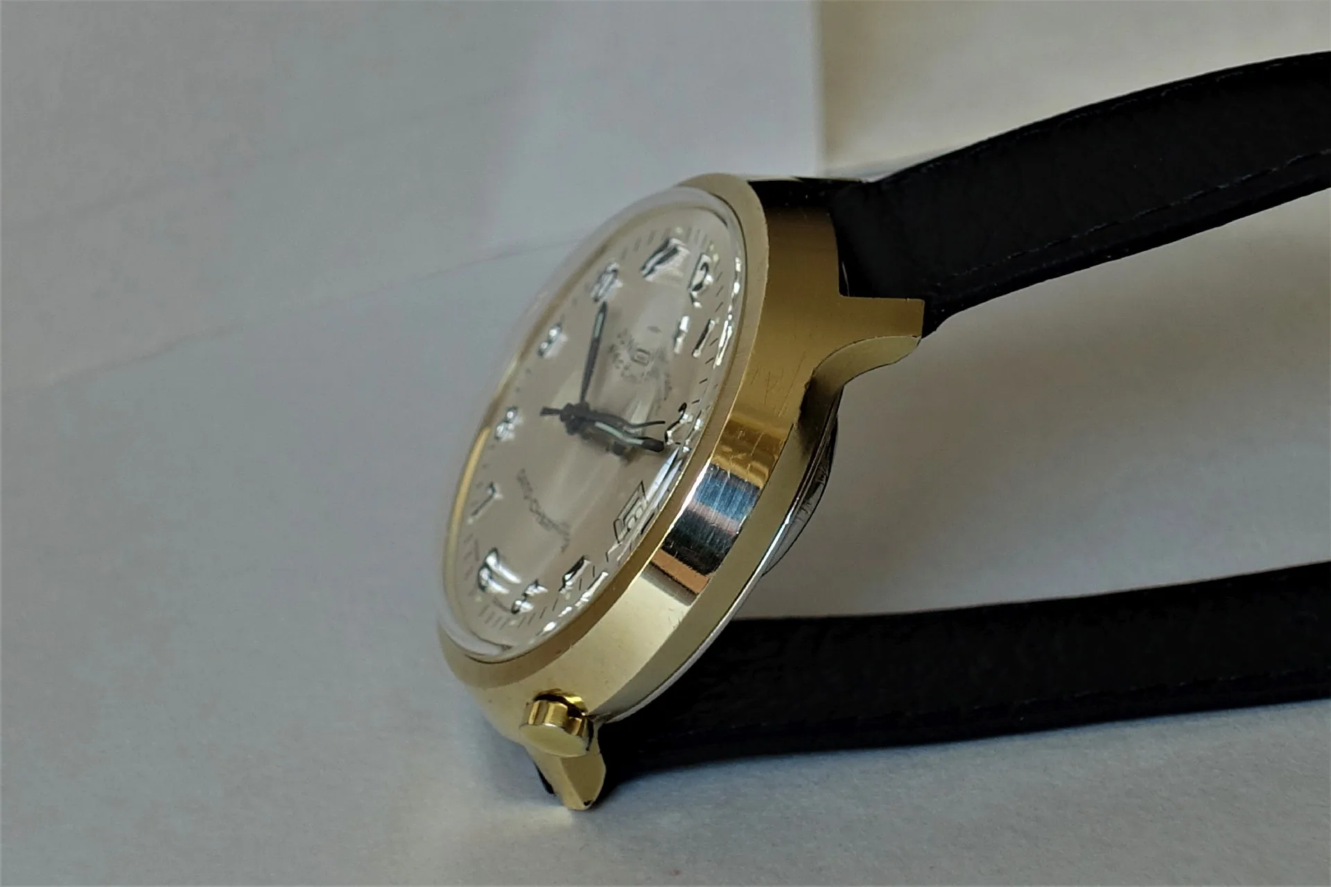 Armbanduhr mit goldfarbenem Gehäuse, hellem Zifferblatt und schwarzem Armband.