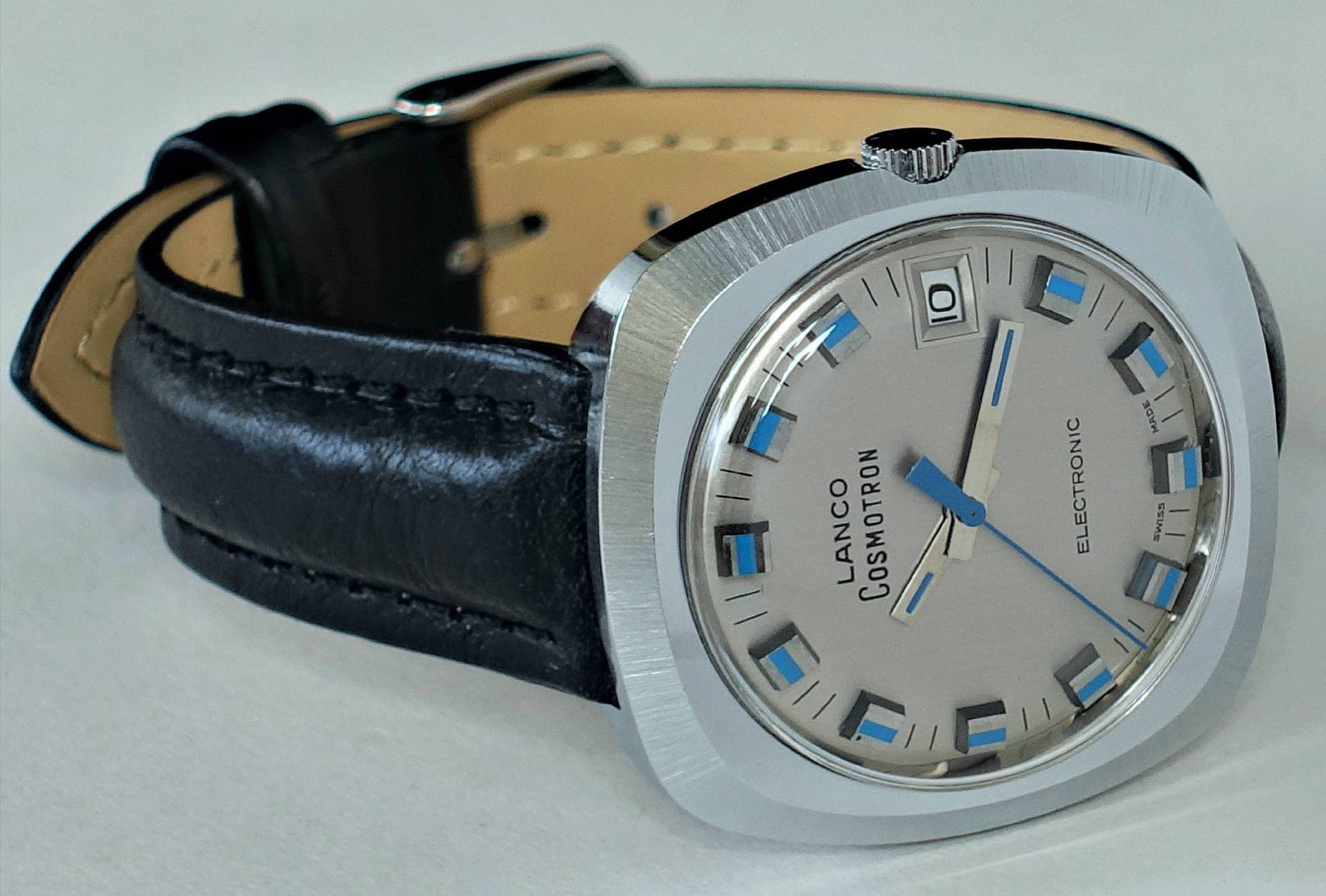 Silberfarbene Armbanduhr mit schwarzem Lederarmband und hellem Zifferblatt mit blauen Akzenten.