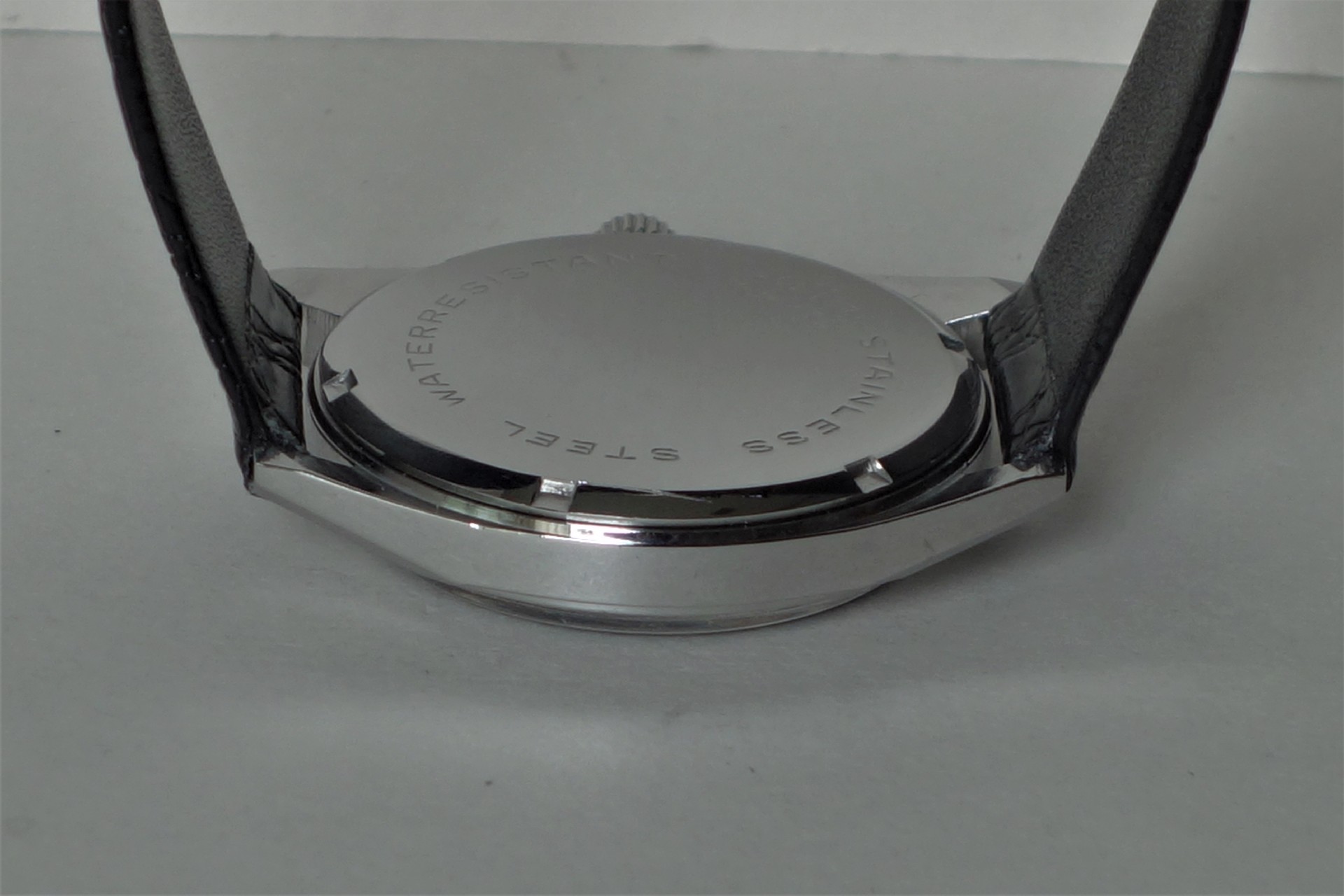 Silberfarbener Uhrenboden mit Gravur und schwarzem Armband.