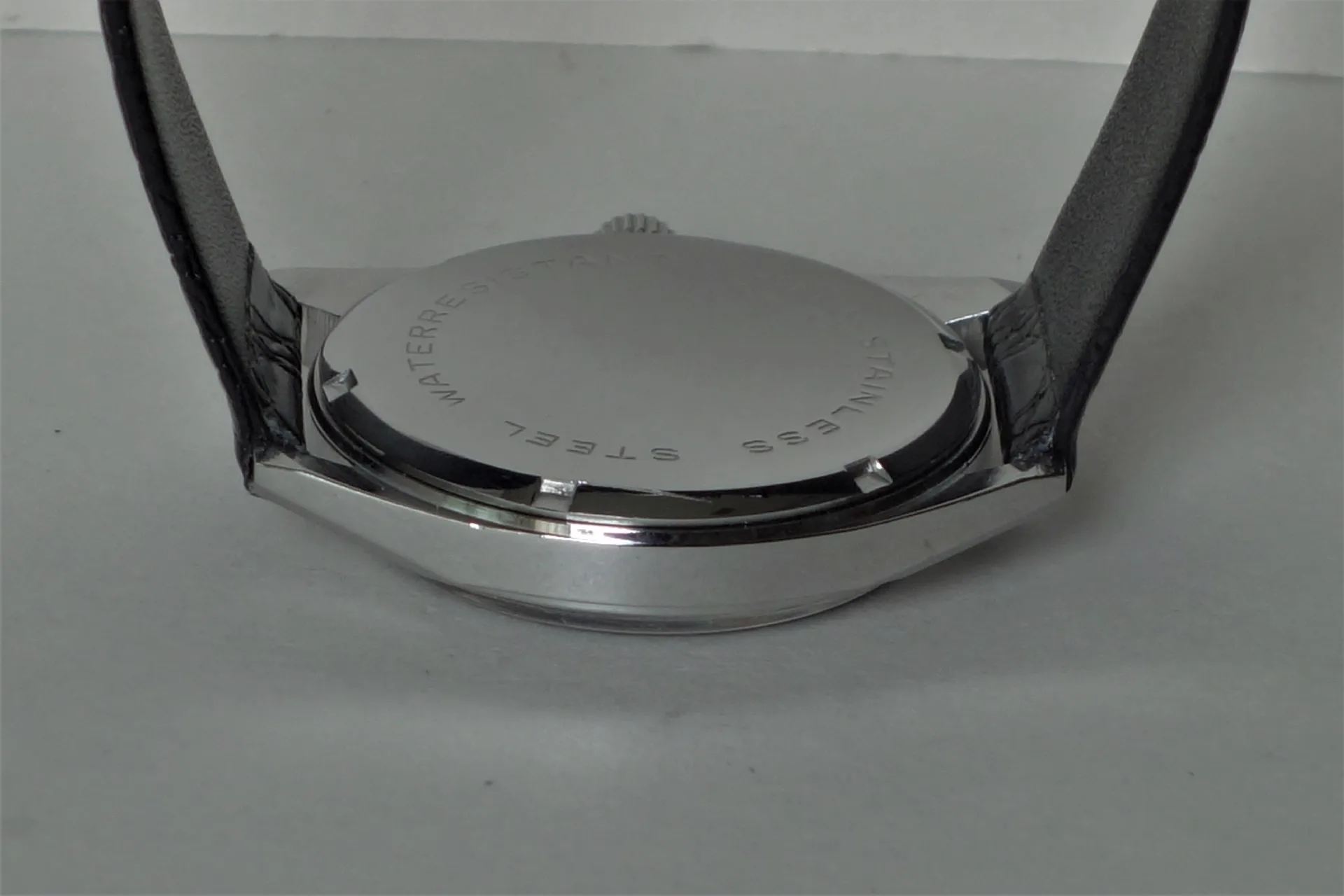 Silberfarbener Uhrenboden mit Gravur und schwarzem Armband.