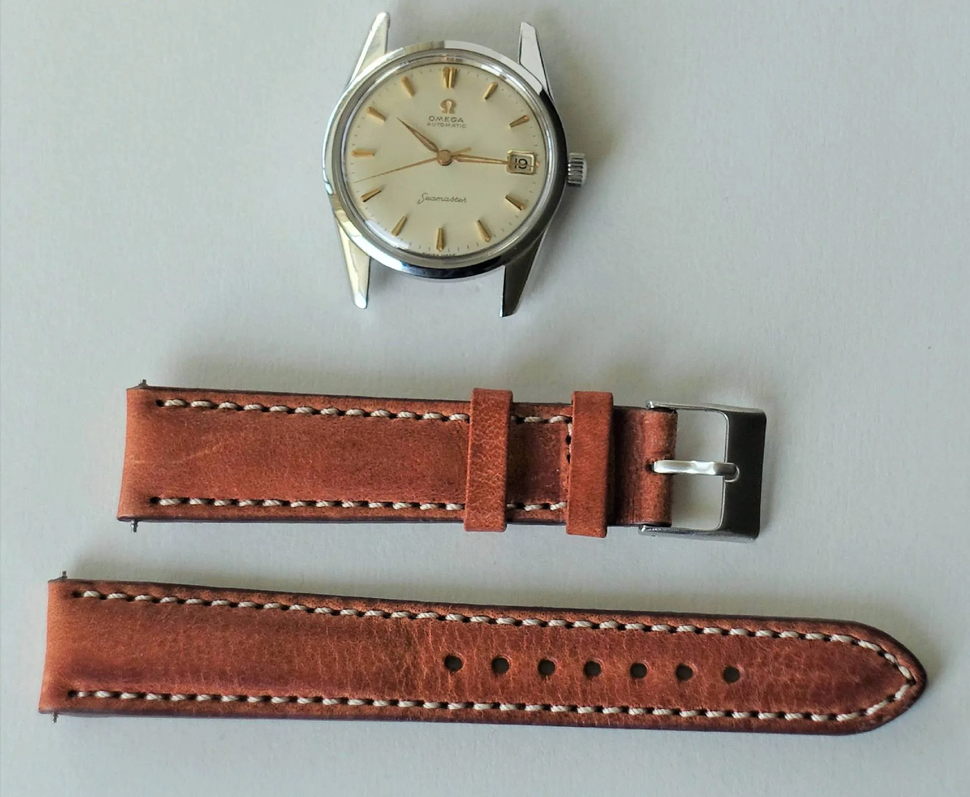 Omega Seamaster Uhrgehäuse Silberfarbenes Uhrgehäuse mit hellem Zifferblatt und goldfarbenen Zeigern, darunter ein braunes Lederarmband in zwei Teilen.