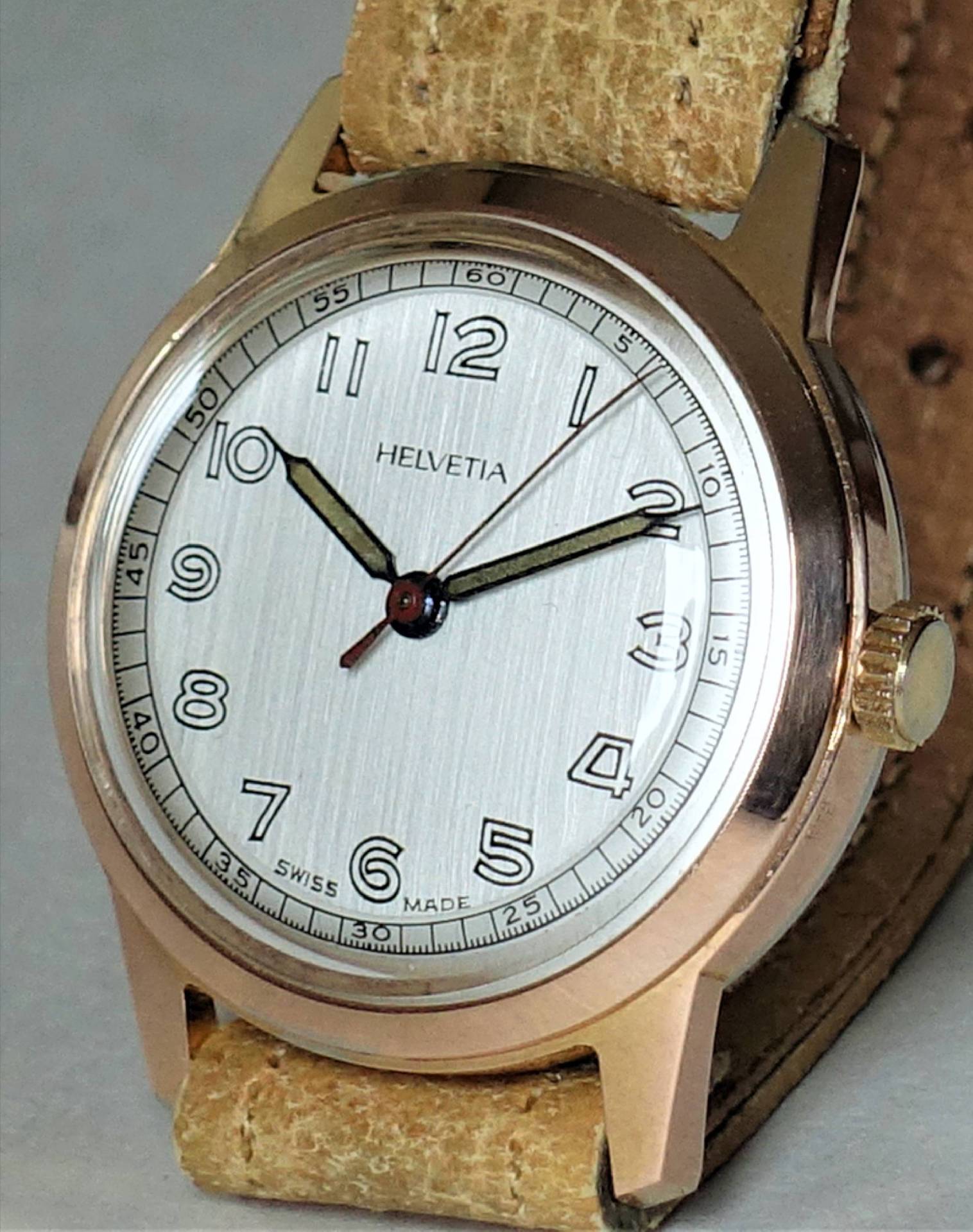 Beige Armbanduhr mit hellem Zifferblatt und schwarzen Zeigern, Gehäuse in goldfarbener Optik.