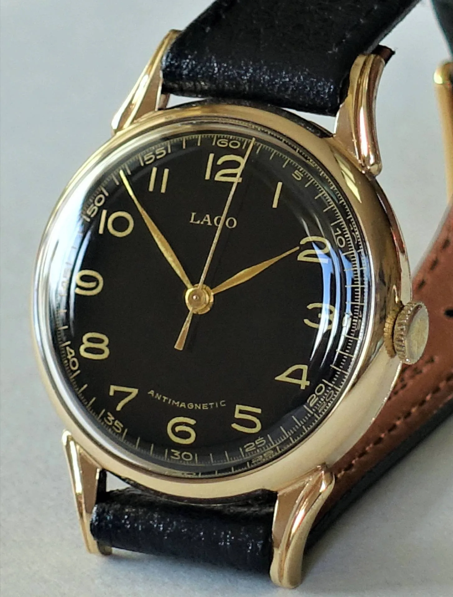 Analoge Armbanduhr mit schwarzem Zifferblatt, goldfarbenem Gehäuse und schwarzem Armband.