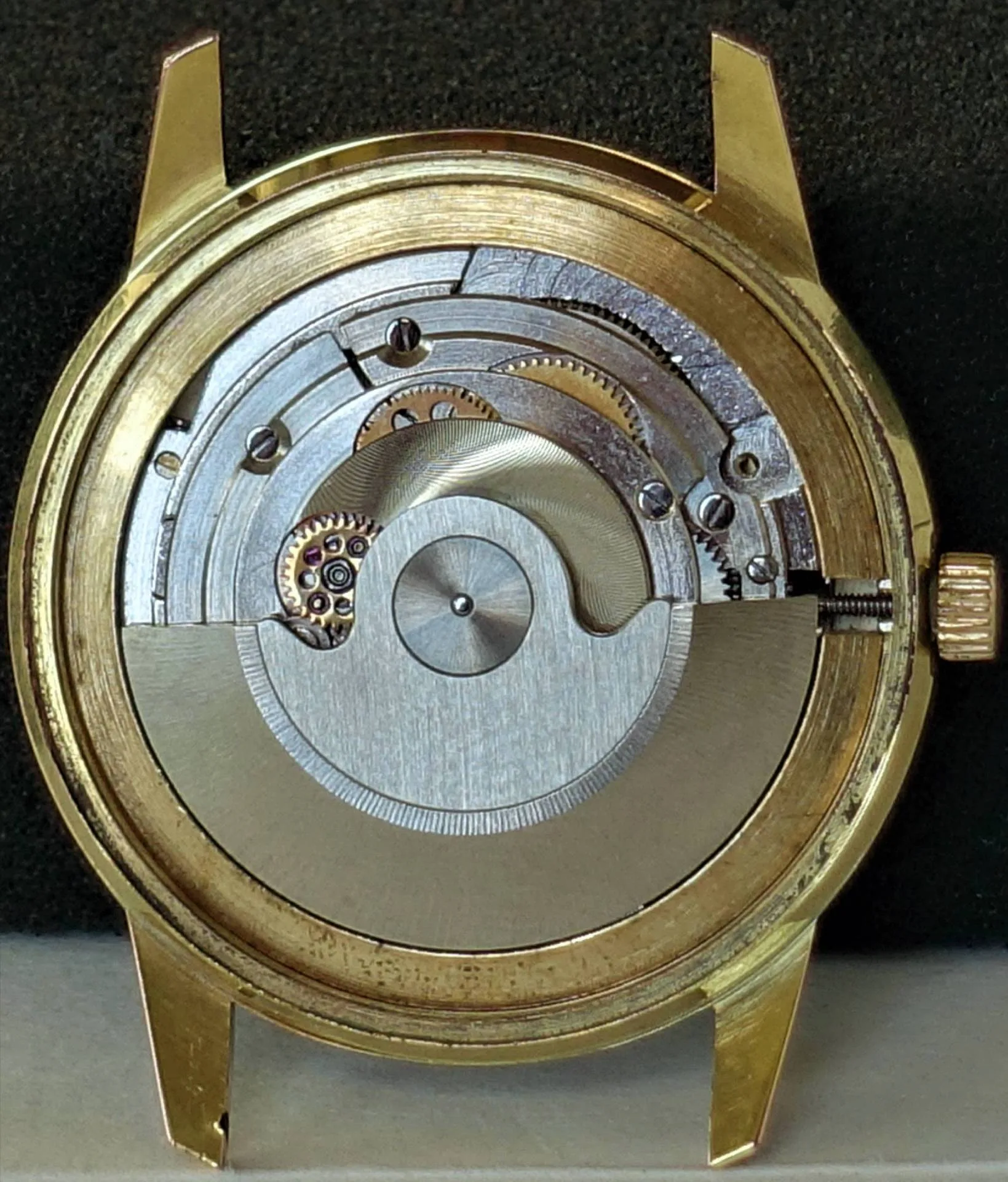 Das Bild zeigt das geöffnete Gehäuse einer Armbanduhr in goldener Farbe mit einem sichtbaren silberfarbenen mechanischen Uhrwerk und Rotor.