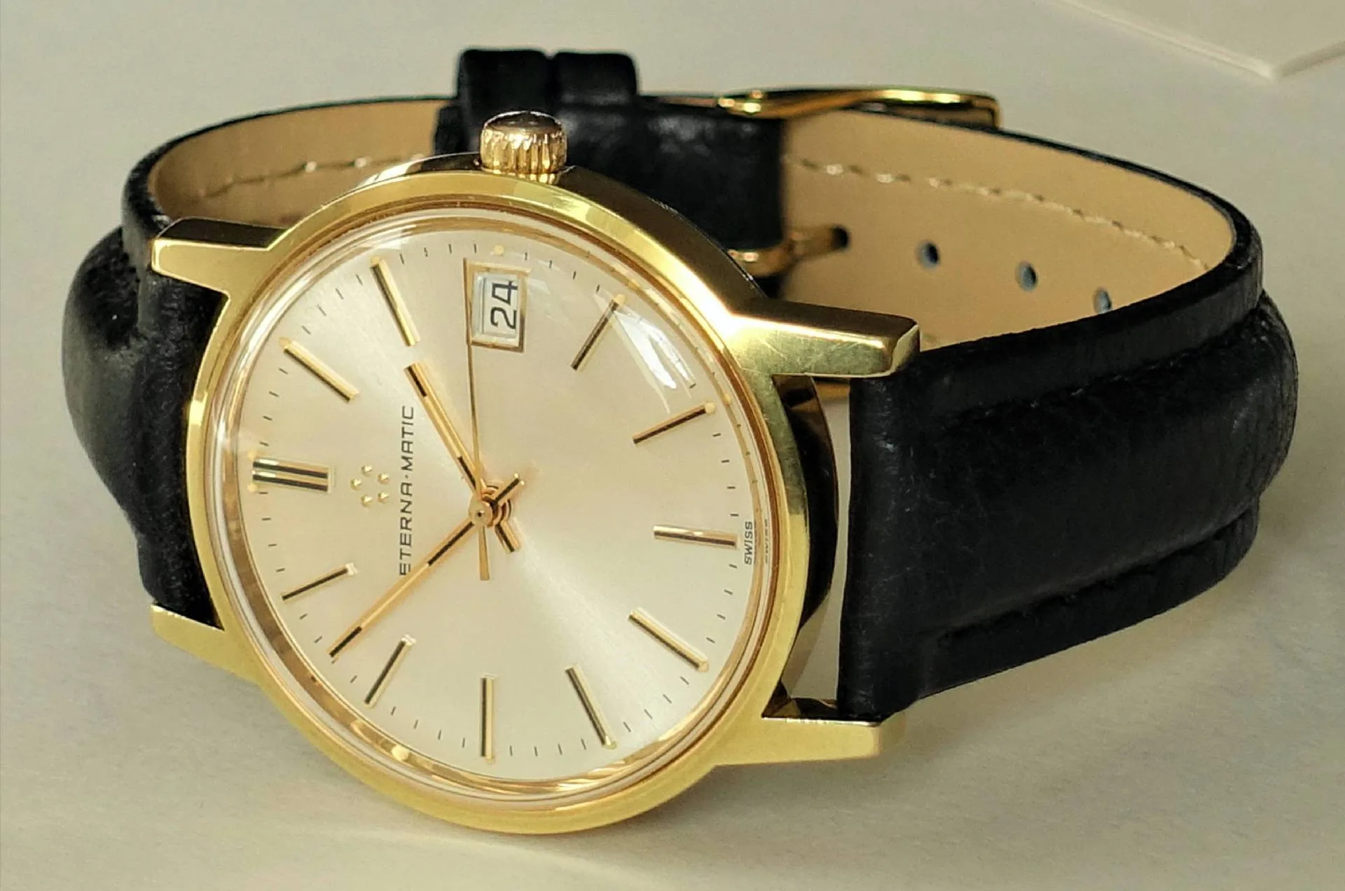 Goldfarbene Armbanduhr mit hellem Zifferblatt und schwarzem Armband.