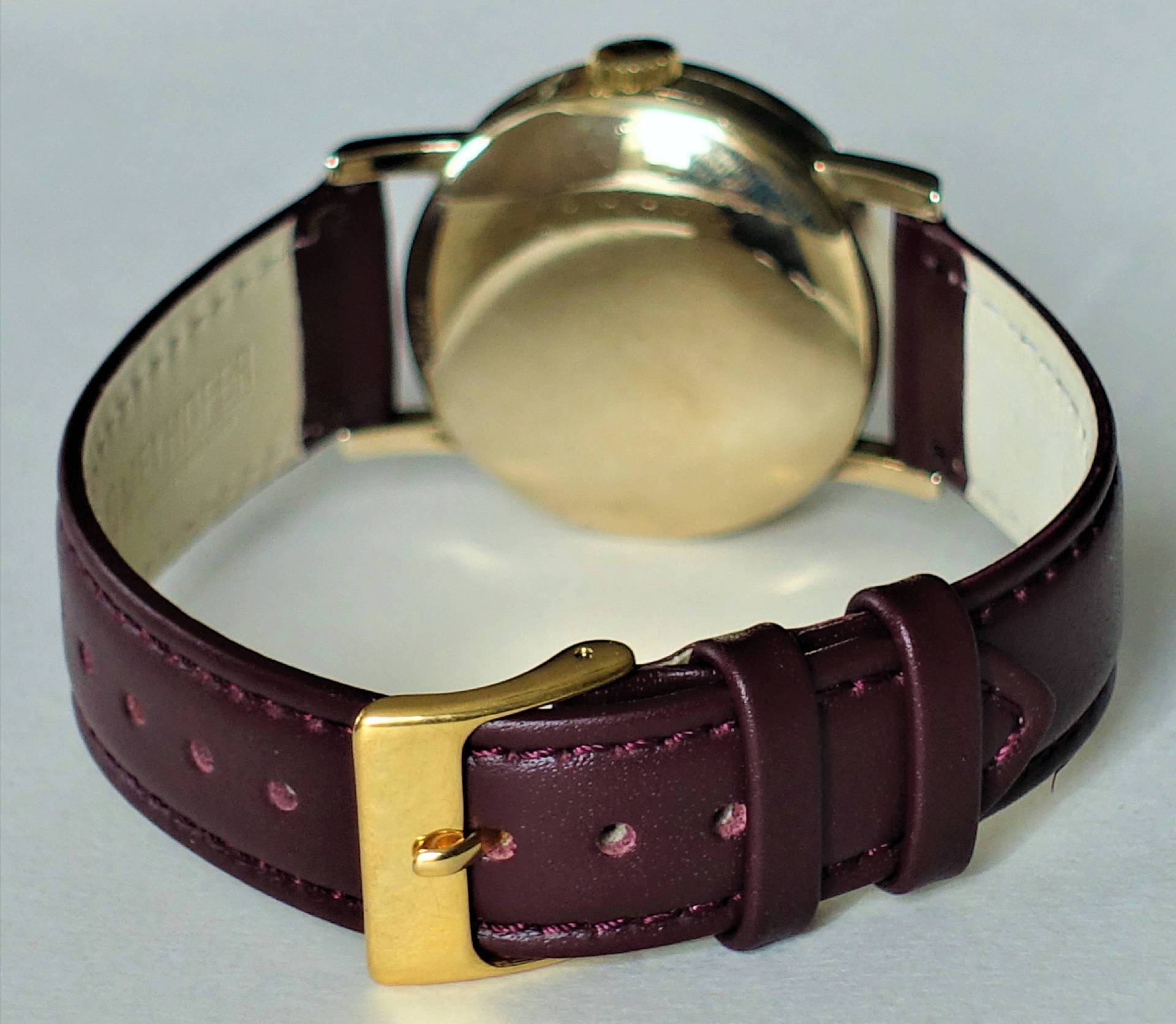 Rückansicht einer eleganten Armbanduhr mit goldener Gehäuse und rotem Lederarmband