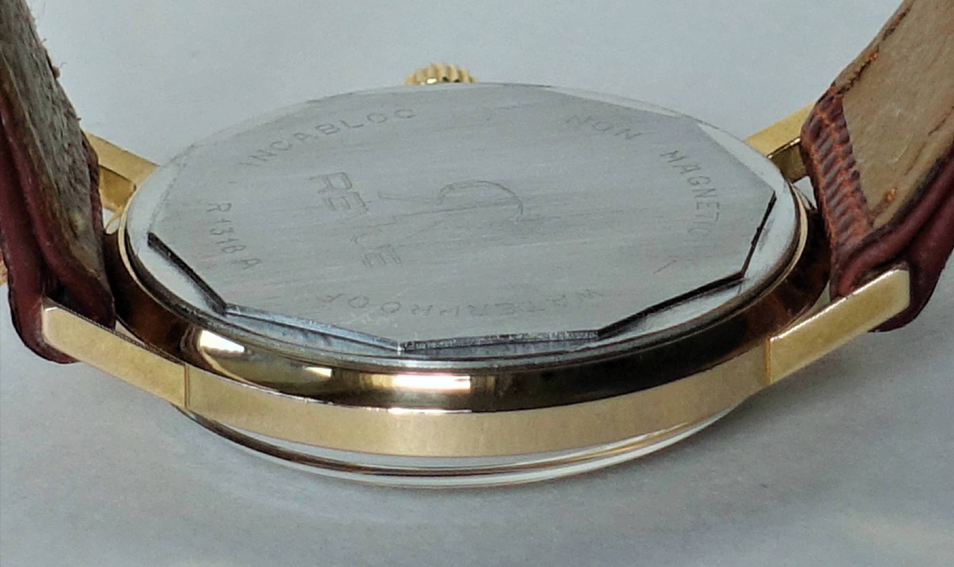 Silberfarbener Uhrboden einer Armbanduhr mit goldfarbenem Gehäuse und braunem Lederarmband.