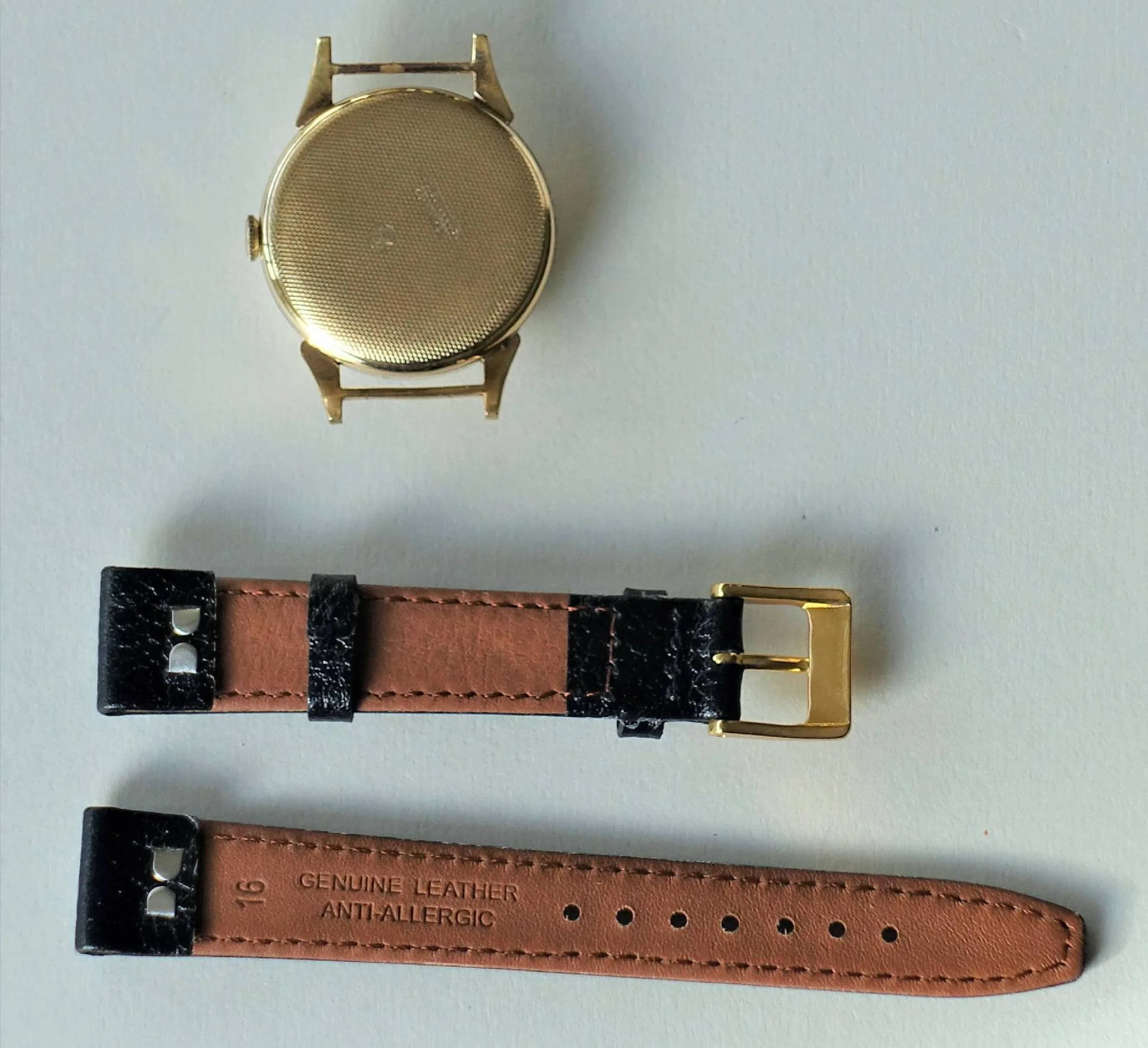 Goldene Uhr mit Lederband Eine goldfarbene Uhr mit abgenommenem schwarz-braunem Lederarmband liegt auf einer hellen Oberfläche.