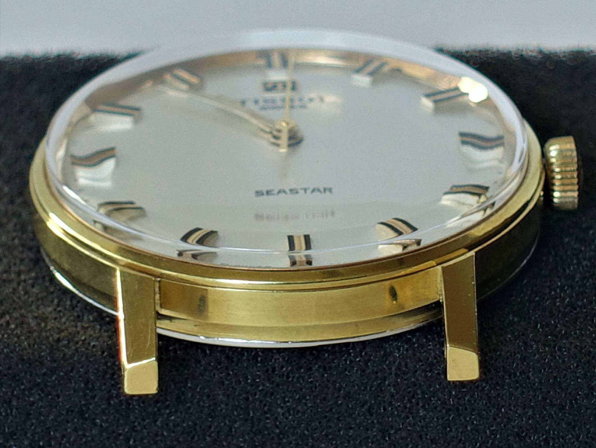 Flache Armbanduhr mit goldfarbenem Gehäuse und hellem Zifferblatt.