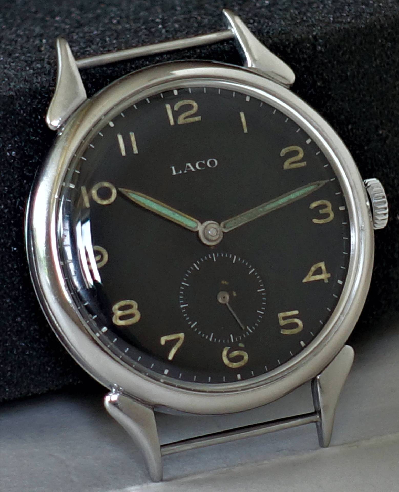 Schwarze Armbanduhr mit silberfarbenem Gehäuse und Leuchtzeigern, Zifferblatt mit arabischen Zahlen.