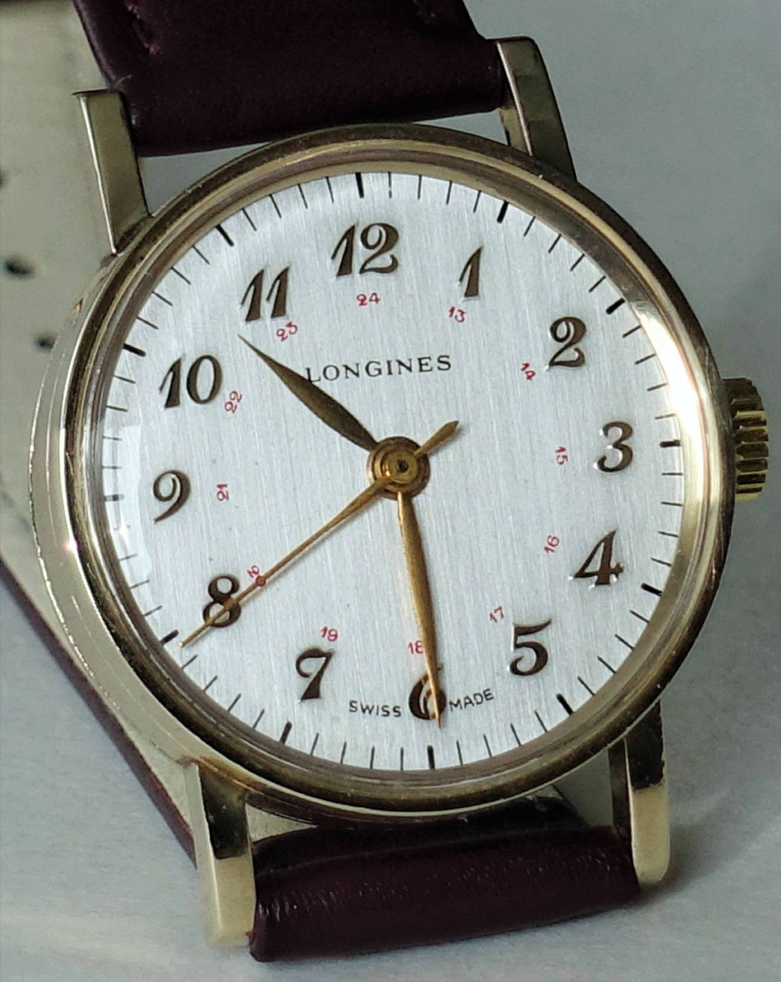 Detailansicht einer eleganten Longines Armbanduhr mit einem weißen Zifferblatt, goldfarbenen Ziffern und einem braunen Lederarmband.