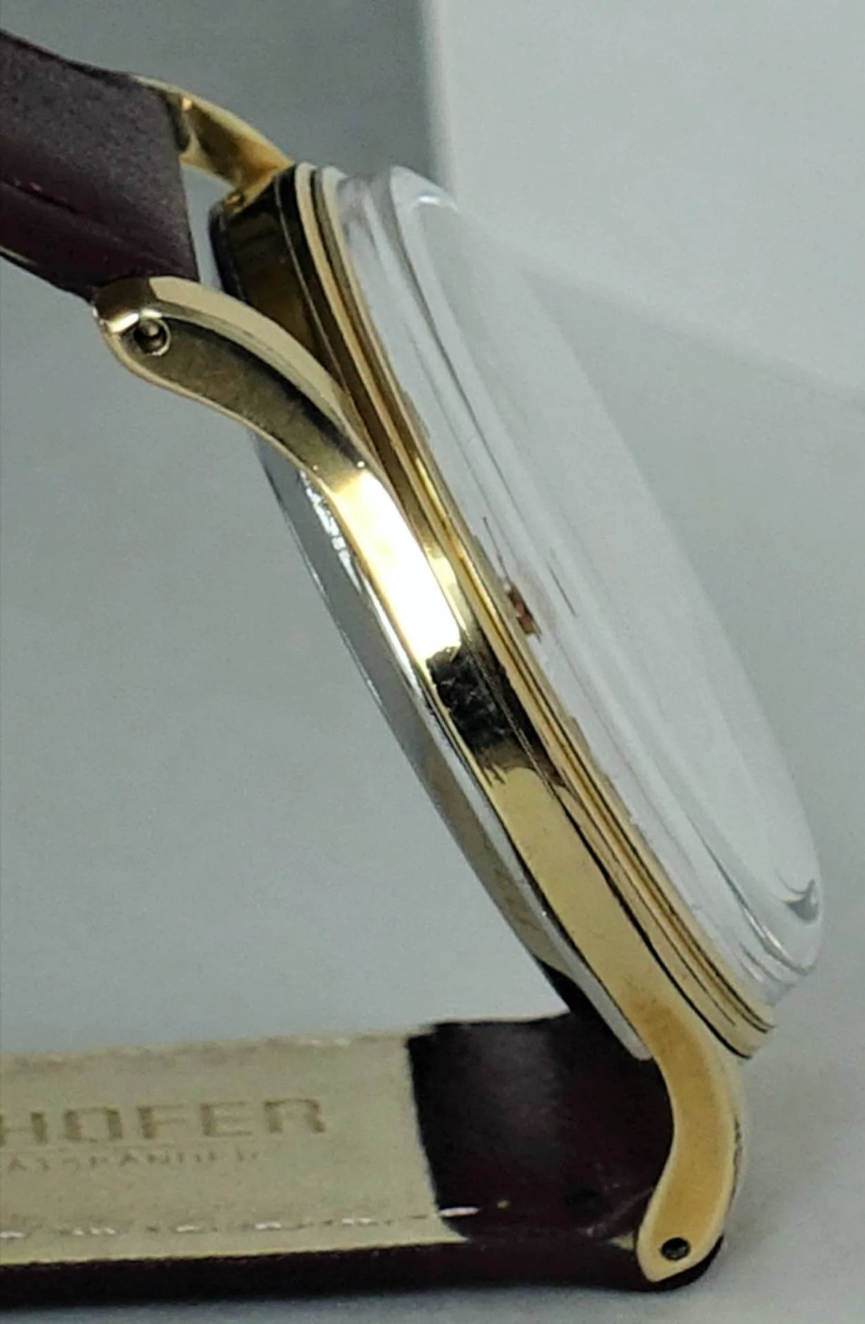 Uhrgehäuse goldfarben Seitliches goldfarbenes Uhrgehäuse mit gewölbtem Glas und braunem Armband.