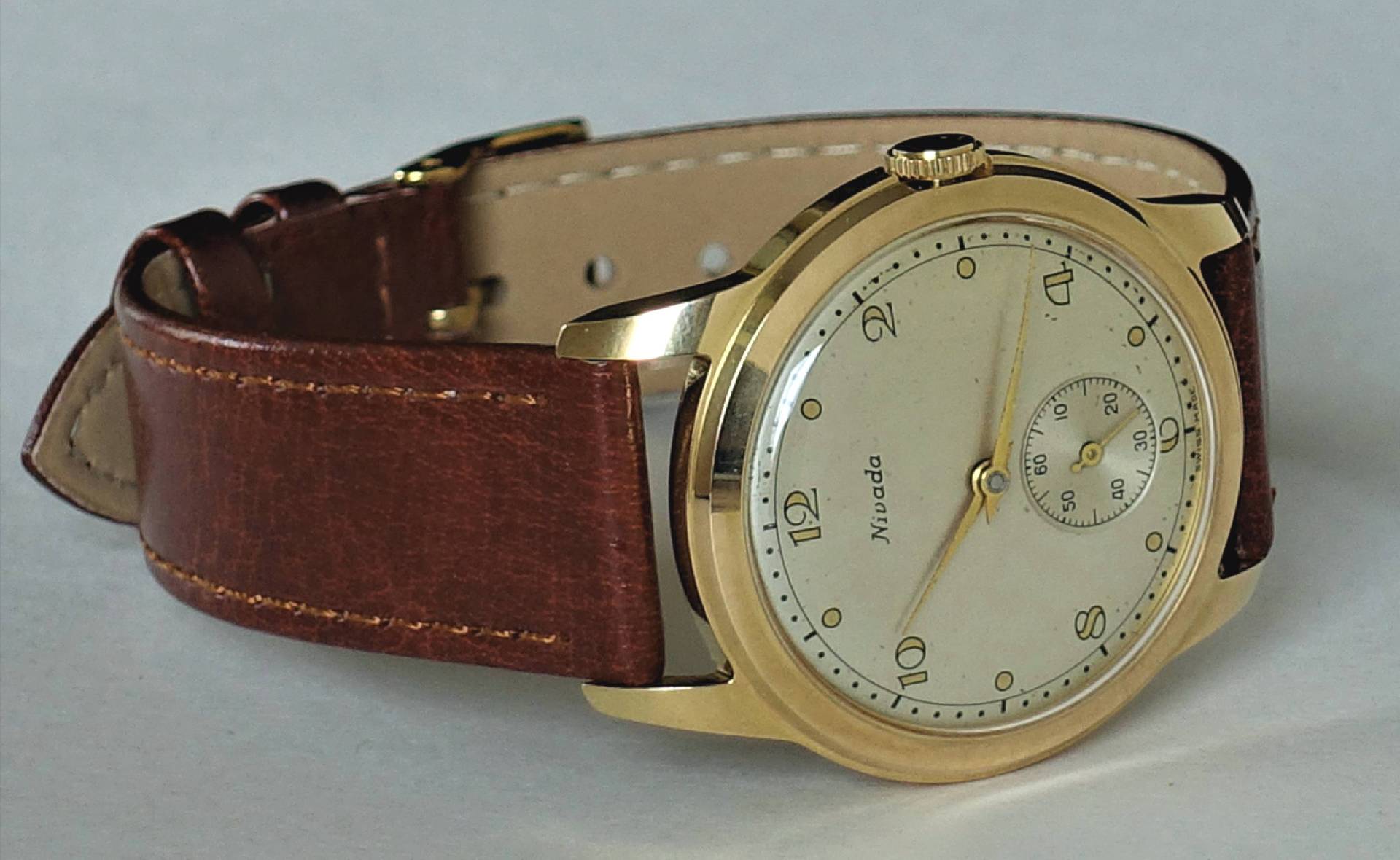 Goldfarbene Armbanduhr mit hellem Zifferblatt und braunem Lederarmband.