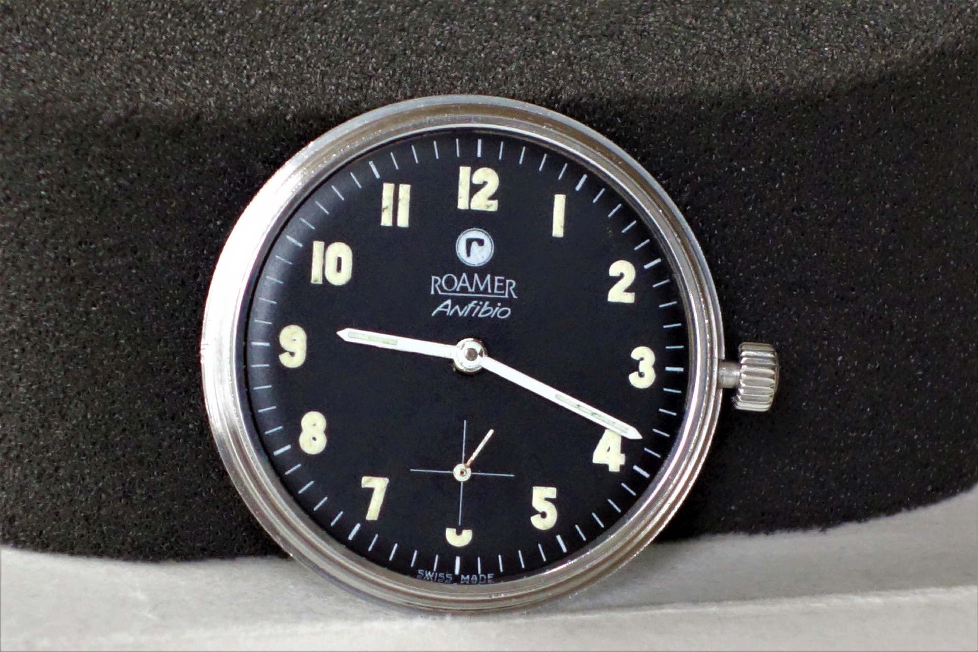 Schwarzes Uhrwerk mit silberfarbenem Rand und Leuchtzeigern, Zifferblatt mit arabischen Zahlen und kleiner Sekunde.