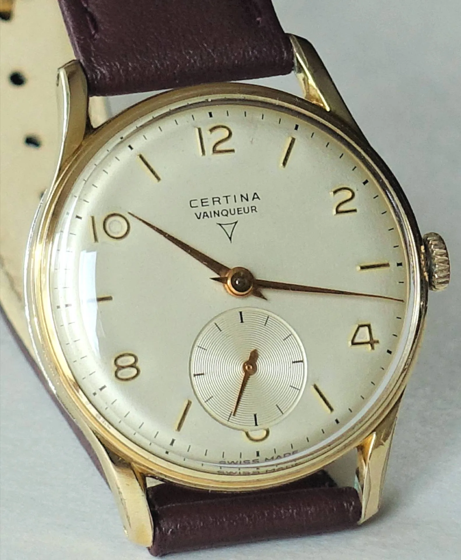 Certina Vainqueur Uhr Klassische Armbanduhr mit hellem Zifferblatt, goldfarbenem Gehäuse und braunem Lederarmband.