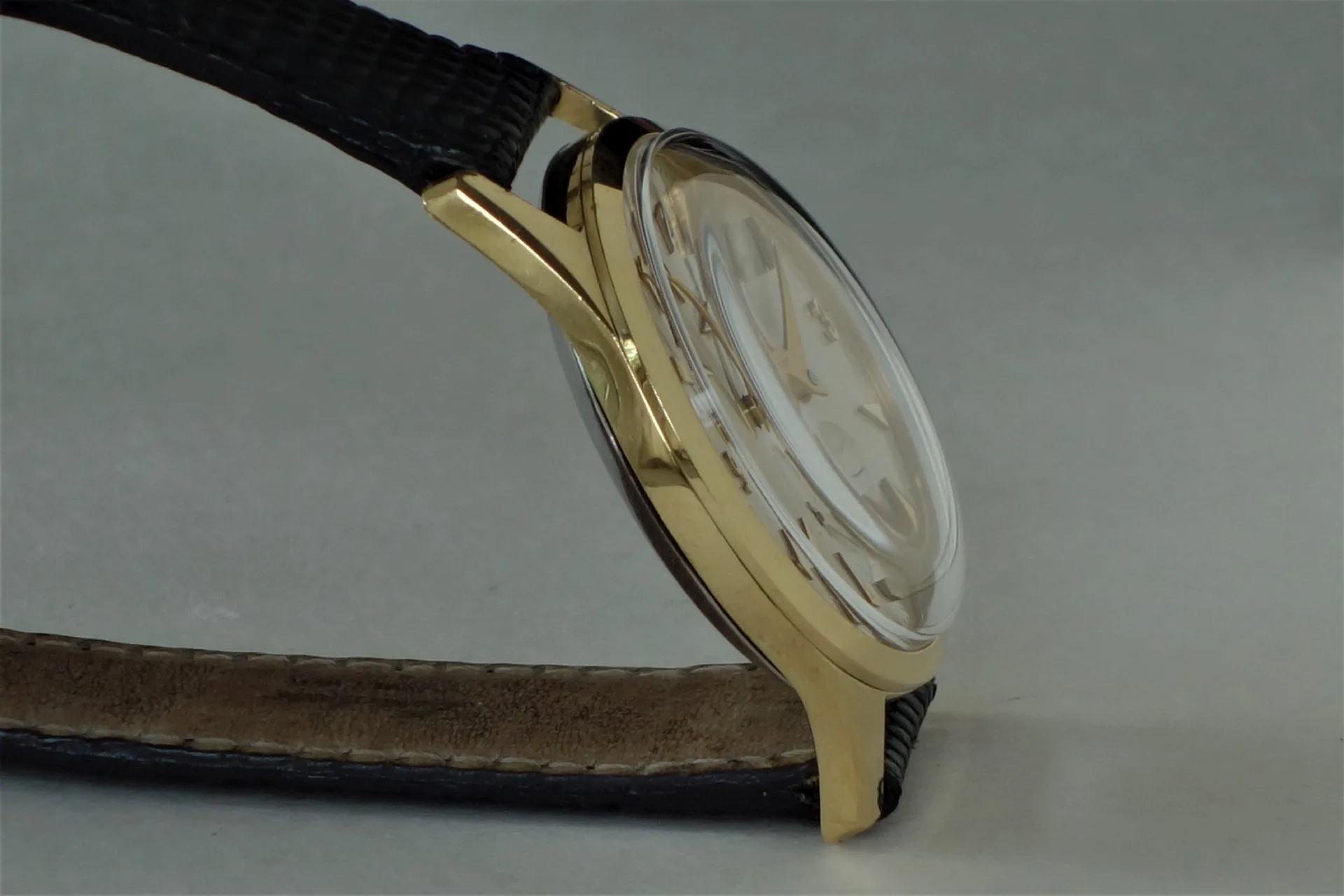 Analoguhr mit goldfarbenem Gehäuse und schwarzem Armband, seitlich fotografiert.