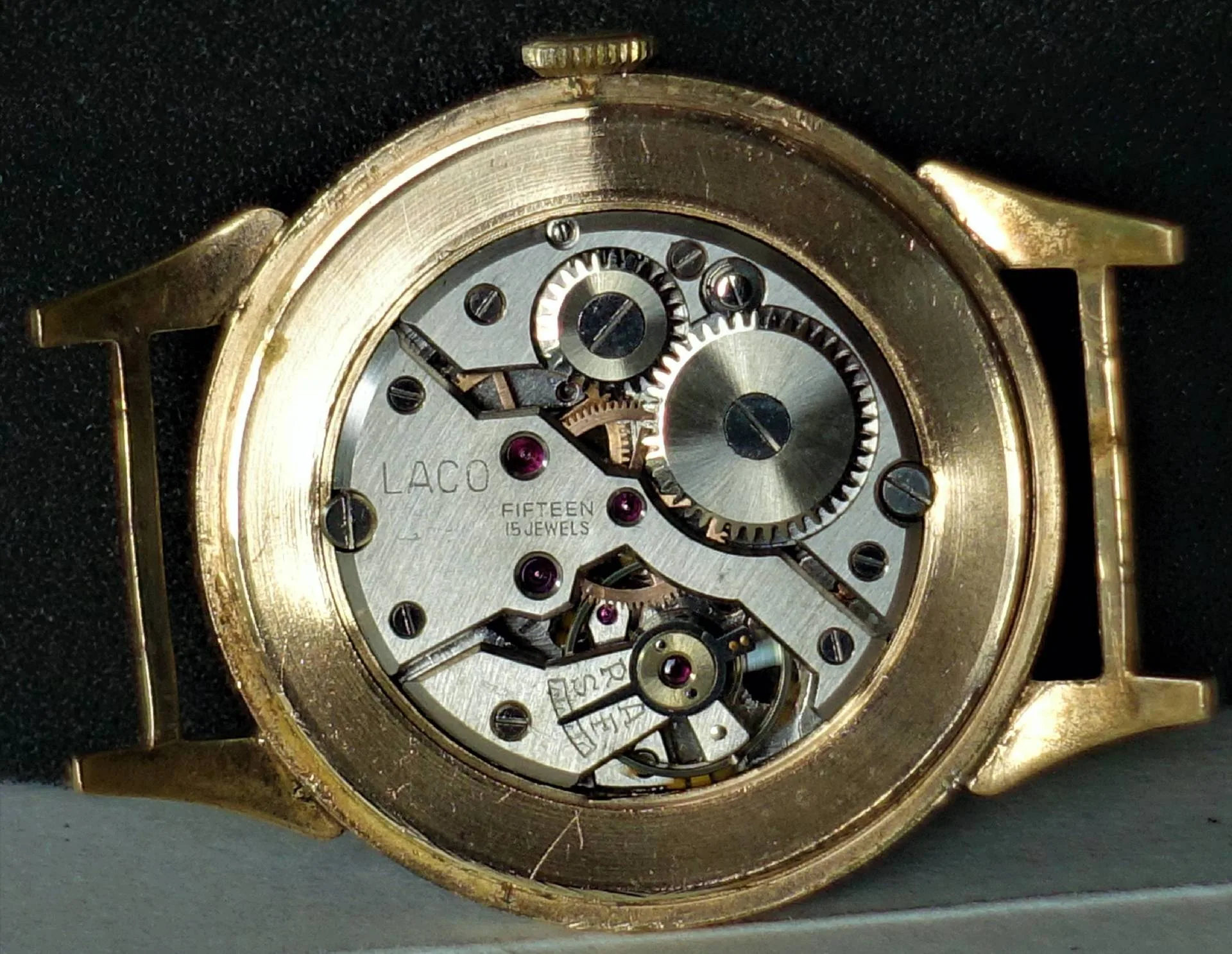 Rückseite einer Armbanduhr mit goldfarbenem Gehäuse und sichtbarem silberfarbenem mechanischem Uhrwerk mit Zahnrädern und roten Lagersteinen.