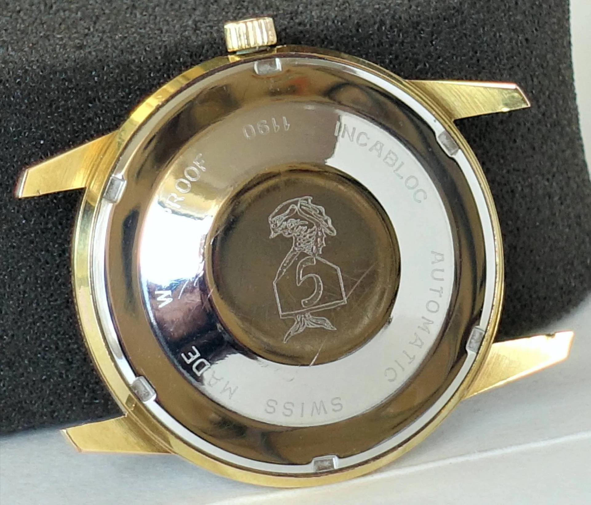 Die Rückseite einer Armbanduhr mit gelb- und silberfarbenem Gehäuse zeigt eine Gravur eines Kopfes sowie umlaufende Gravuren mit technischen Angaben.