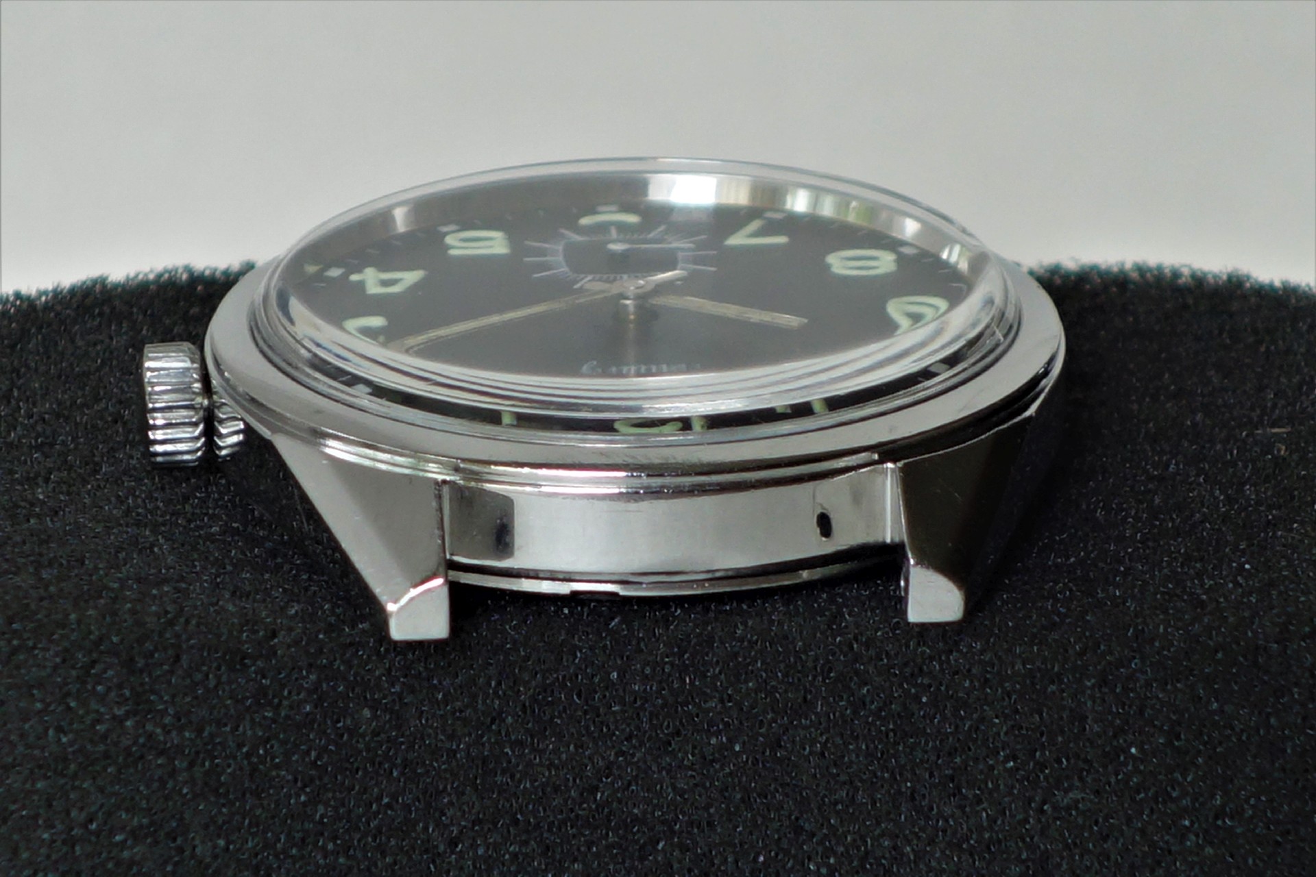 Schwarzes Uhrgehäuse mit Zifferblatt und Zeigern, ohne Armband, silberfarbene Krone.