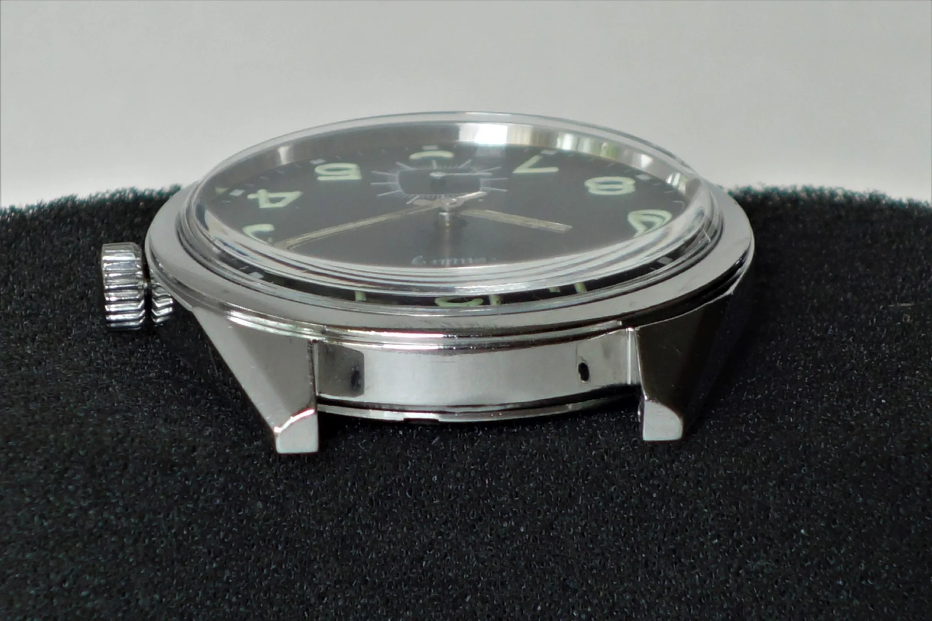 Schwarzes Uhrgehäuse mit Zifferblatt und Zeigern, ohne Armband, silberfarbene Krone.