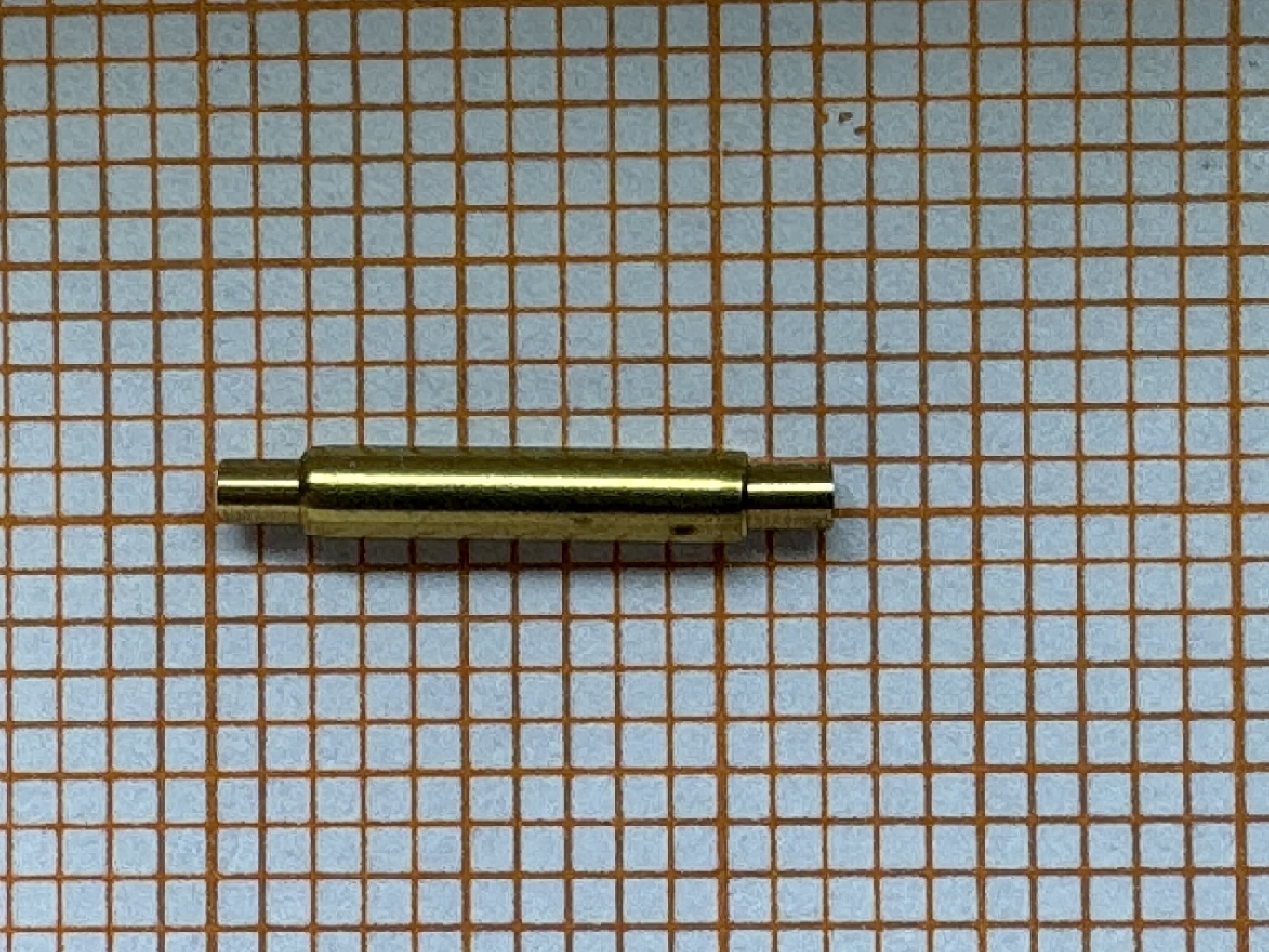 Zylindrische Aufzugswelle aus Metall für Uhrwerke, auf kariertem Papier liegend.