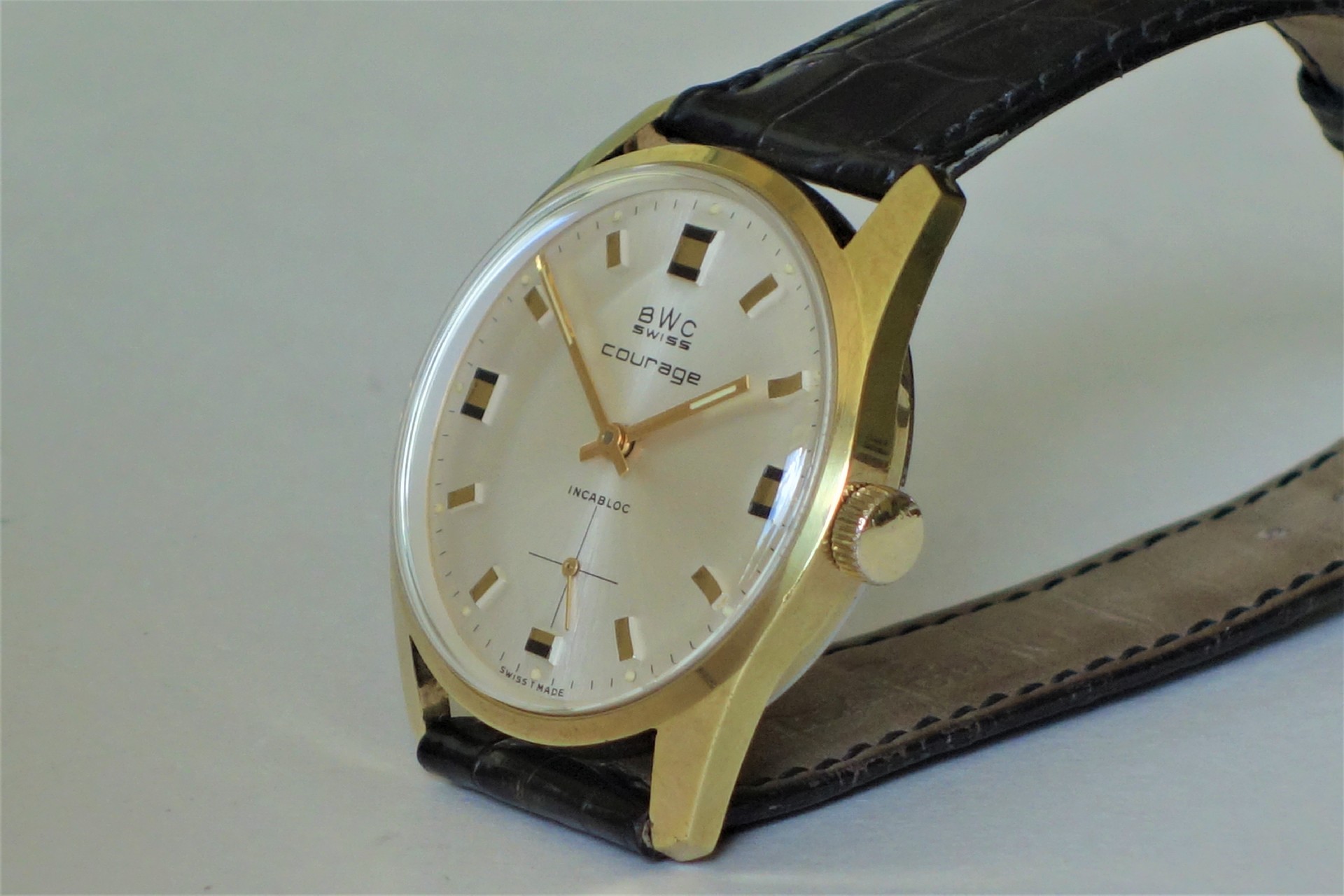 Goldfarbene Armbanduhr mit hellem Zifferblatt und schwarzem Lederarmband.