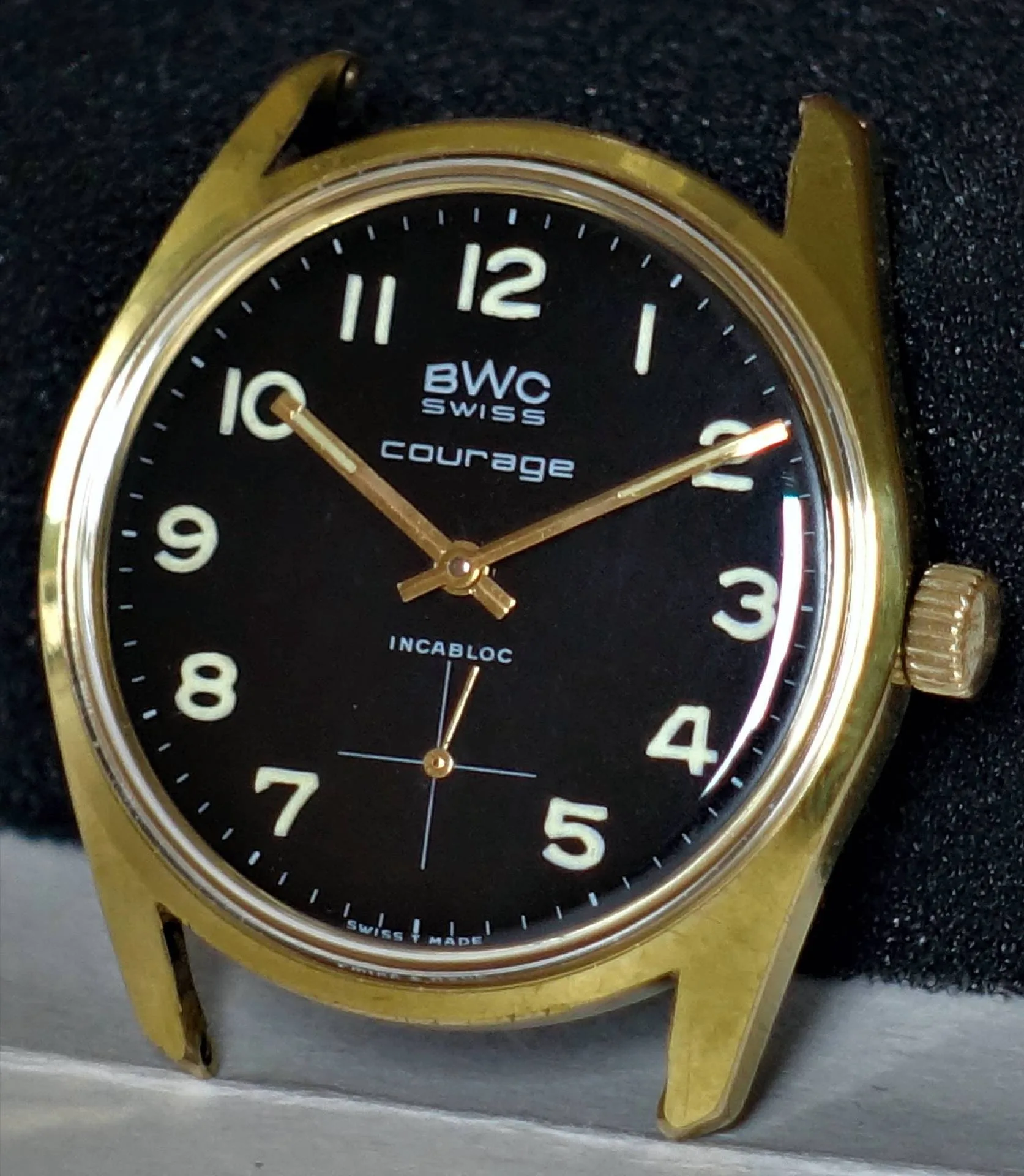 Schwarze Armbanduhr mit goldfarbenem Gehäuse und Leuchtziffern.