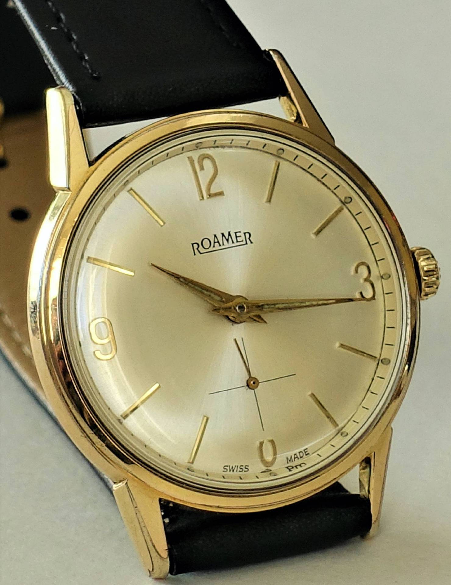 Goldfarbene Armbanduhr mit hellem Zifferblatt und schwarzem Armband.