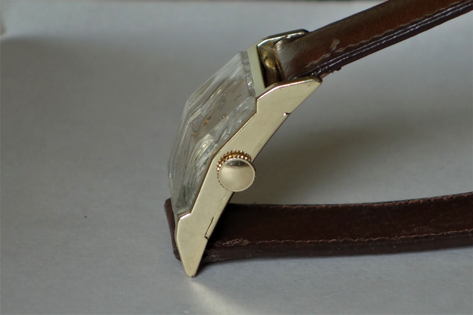 Rechteckige Armbanduhr mit braunem Armband und hellem Gehäuse.