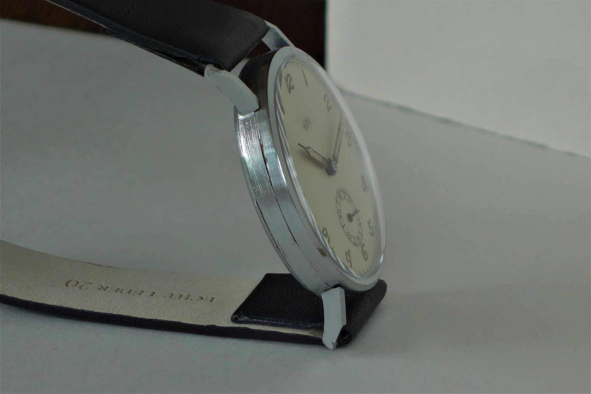 Analoge Armbanduhr mit silberfarbenem Gehäuse, hellem Zifferblatt und schwarzem Armband.