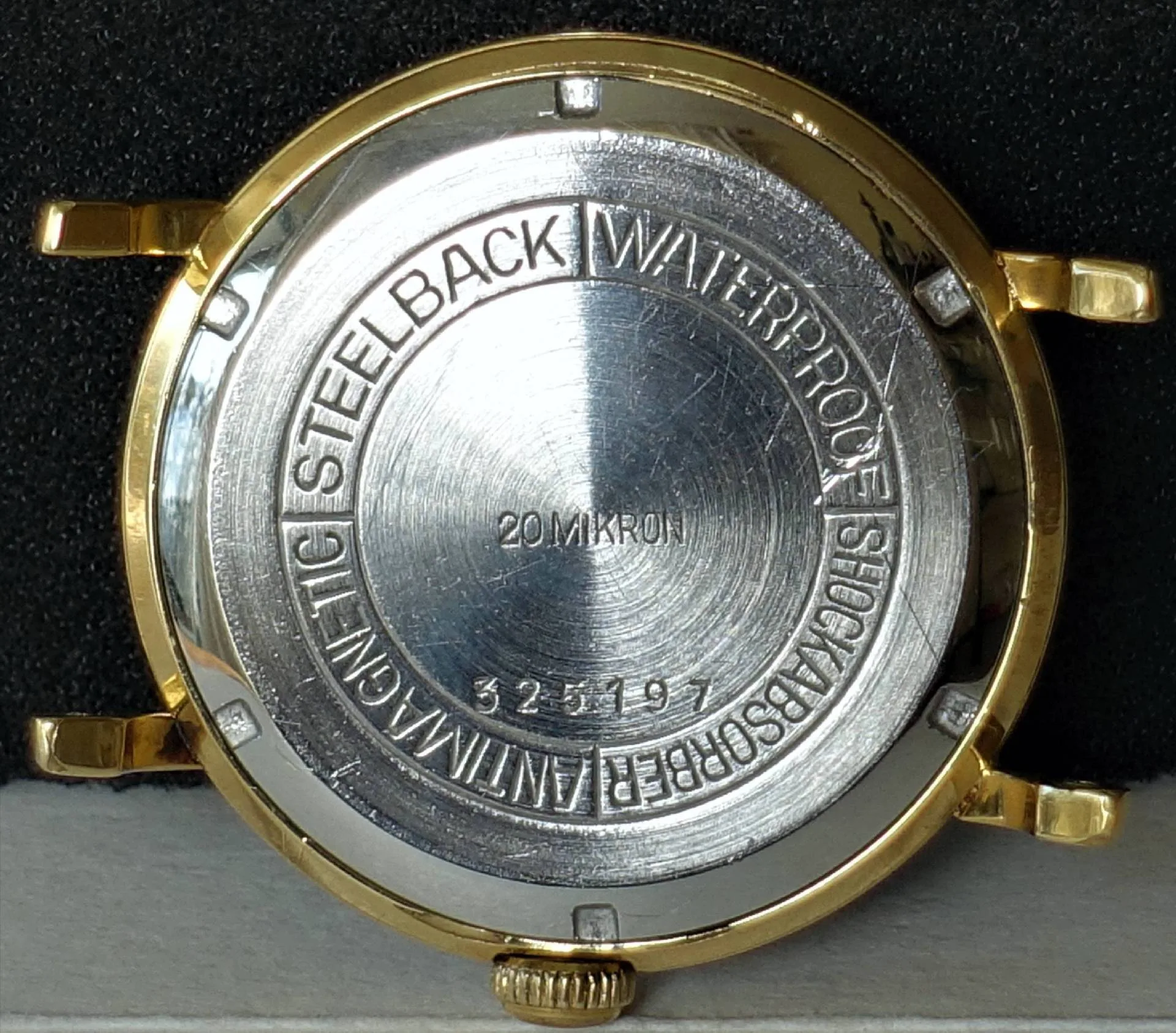 Silberfarbene Rückseite eines Uhrengehäuses mit Gravur und goldfarbenem Rand.