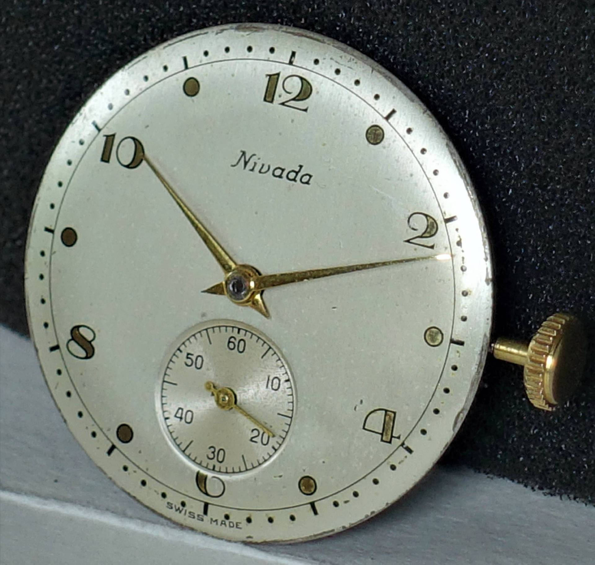 Rundes helles Zifferblatt mit goldfarbenen Zeigern und kleiner Sekunde, seitlich goldene Krone.