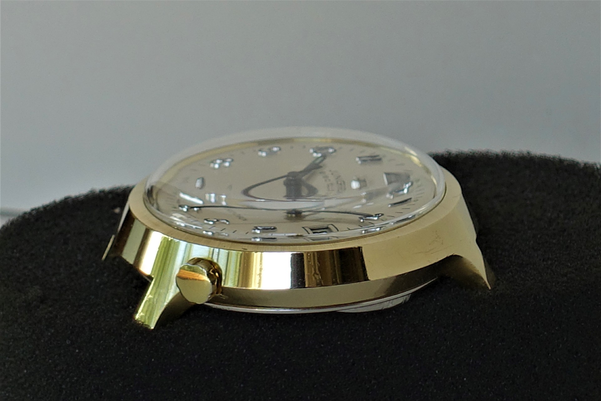 Goldfarbenes Uhrgehäuse mit montiertem Zifferblatt und Zeigern, seitliche Ansicht.