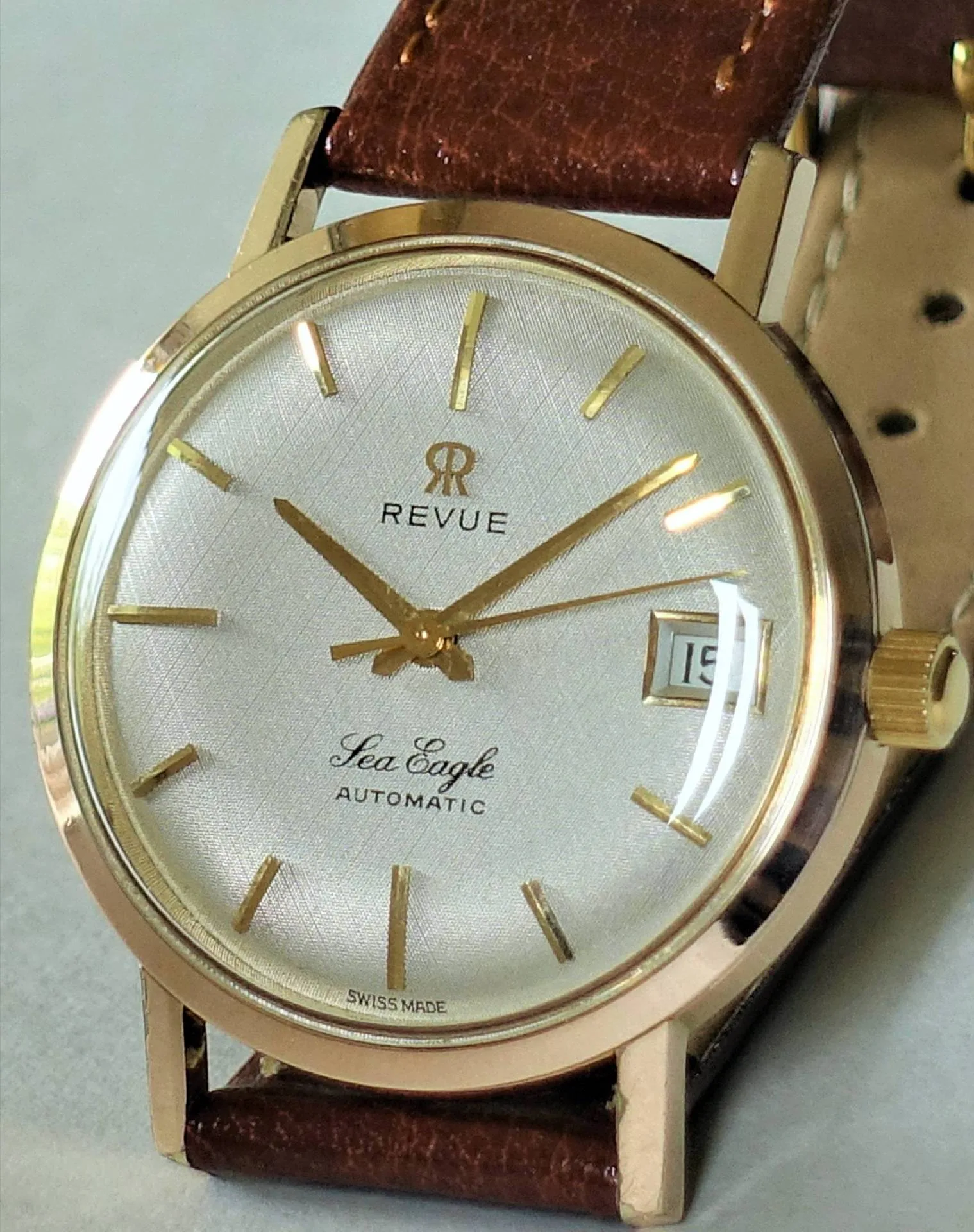 Revue Sea Eagle Automatikuhr Goldfarbene Armbanduhr mit silbernem Zifferblatt, braunem Armband und Datumsanzeige.