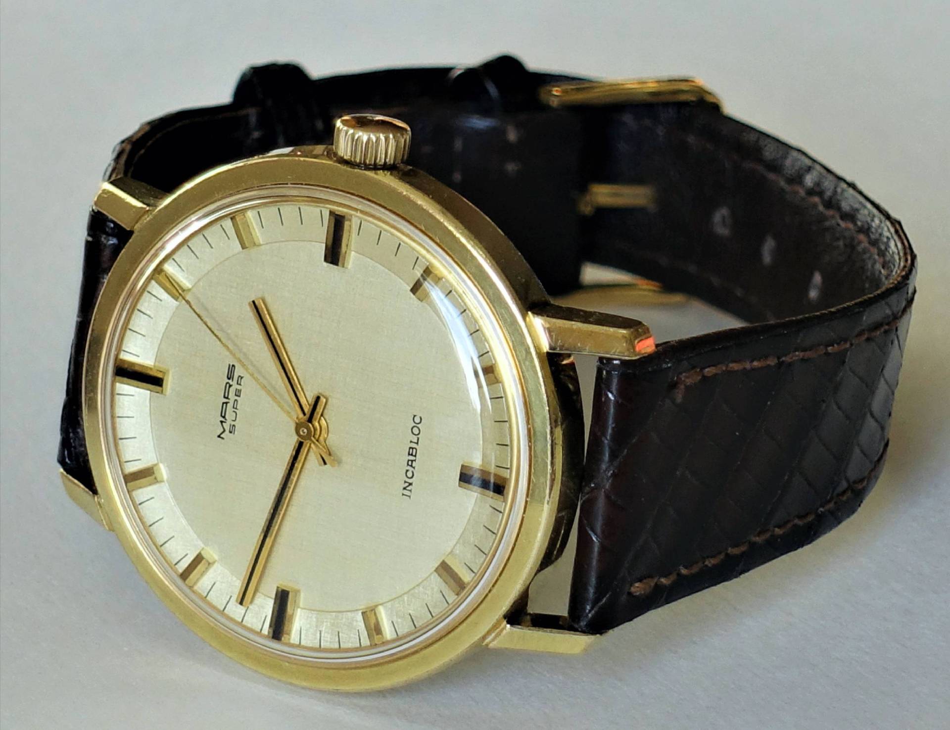 Goldfarbene Armbanduhr mit hellem Zifferblatt und braunem Lederarmband.