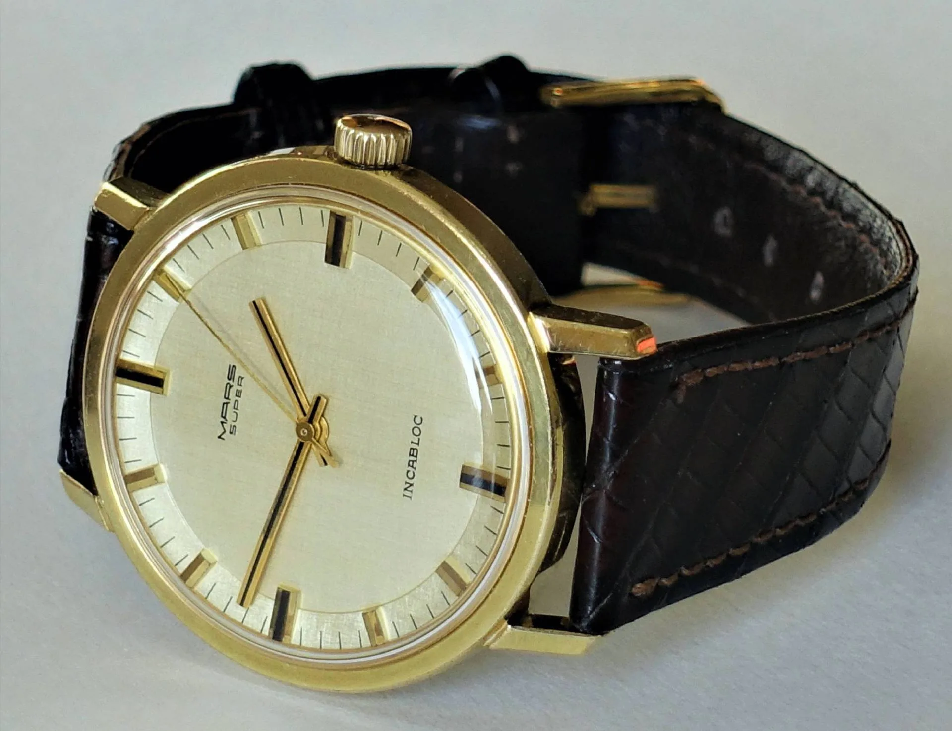 Mars Super Armbanduhr Goldfarbene Armbanduhr mit hellem Zifferblatt und braunem Lederarmband.