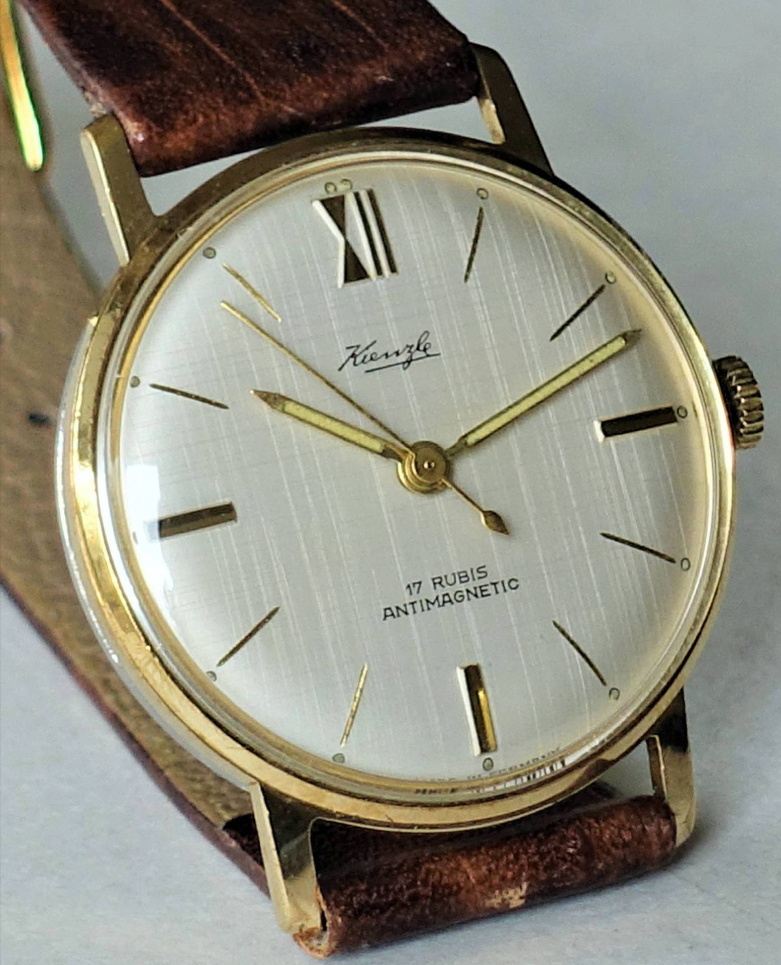 Goldfarbene Armbanduhr mit weißem Zifferblatt und braunem Armband.