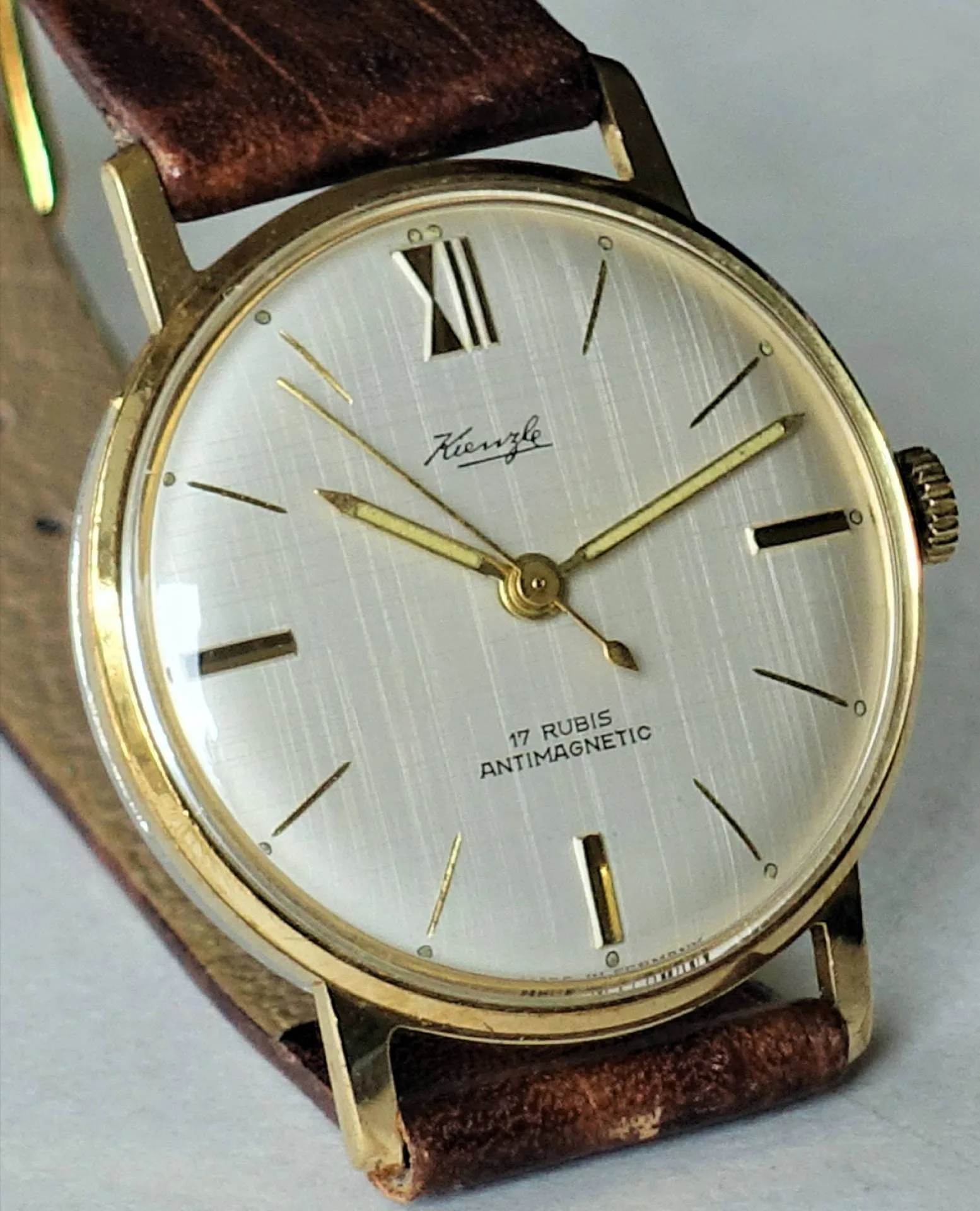 Goldfarbene Armbanduhr mit weißem Zifferblatt und braunem Armband.