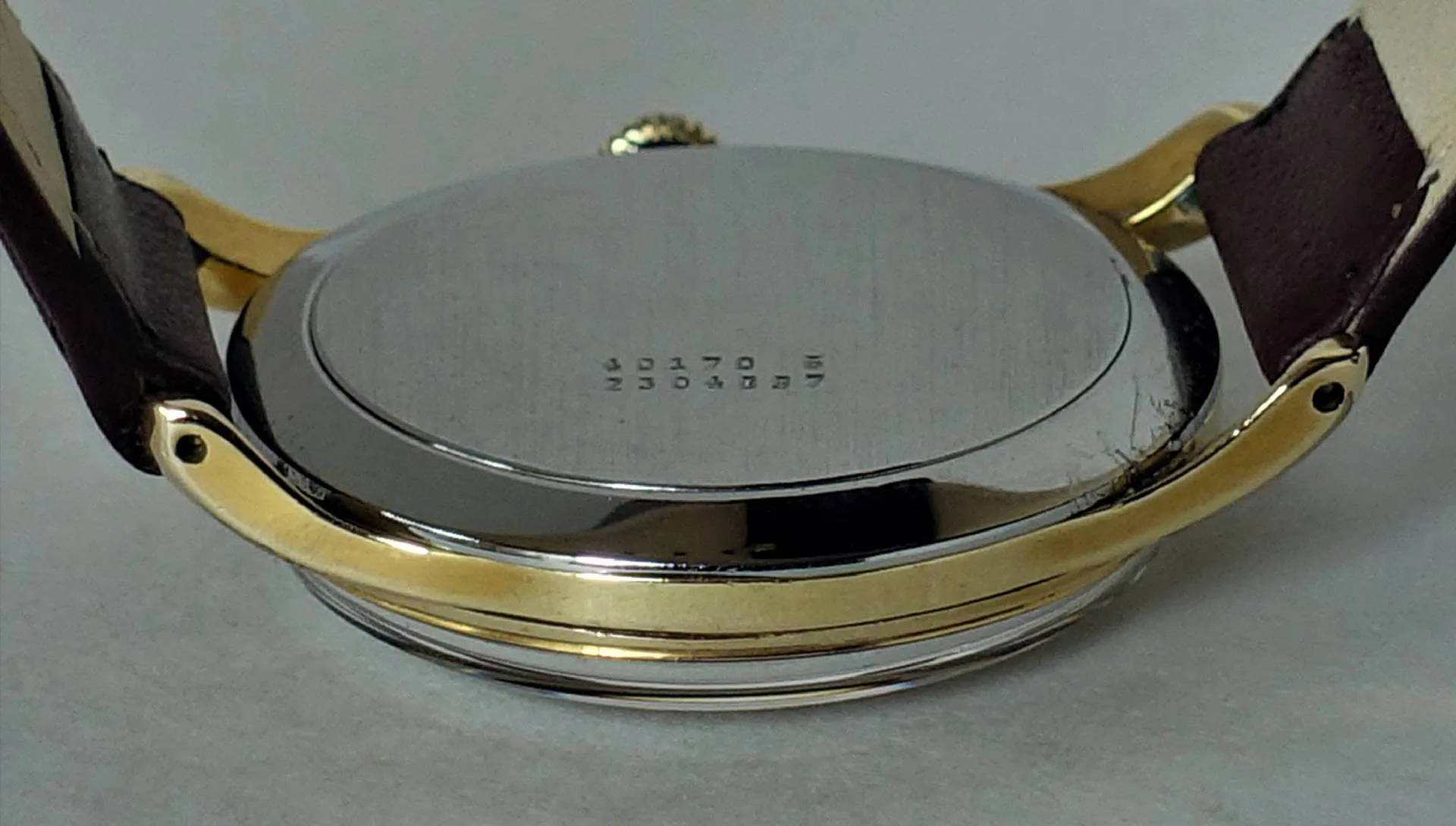 Uhrenboden silberfarben Runder silberfarbener Uhrenboden mit Gravur, montiert an einem Gehäuse mit braunem Armband.
