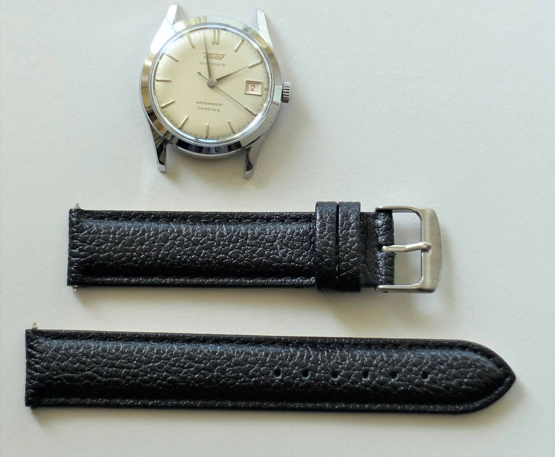 Silberfarbene Armbanduhr mit hellem Zifferblatt und schwarzem Lederarmband in zwei Teilen.