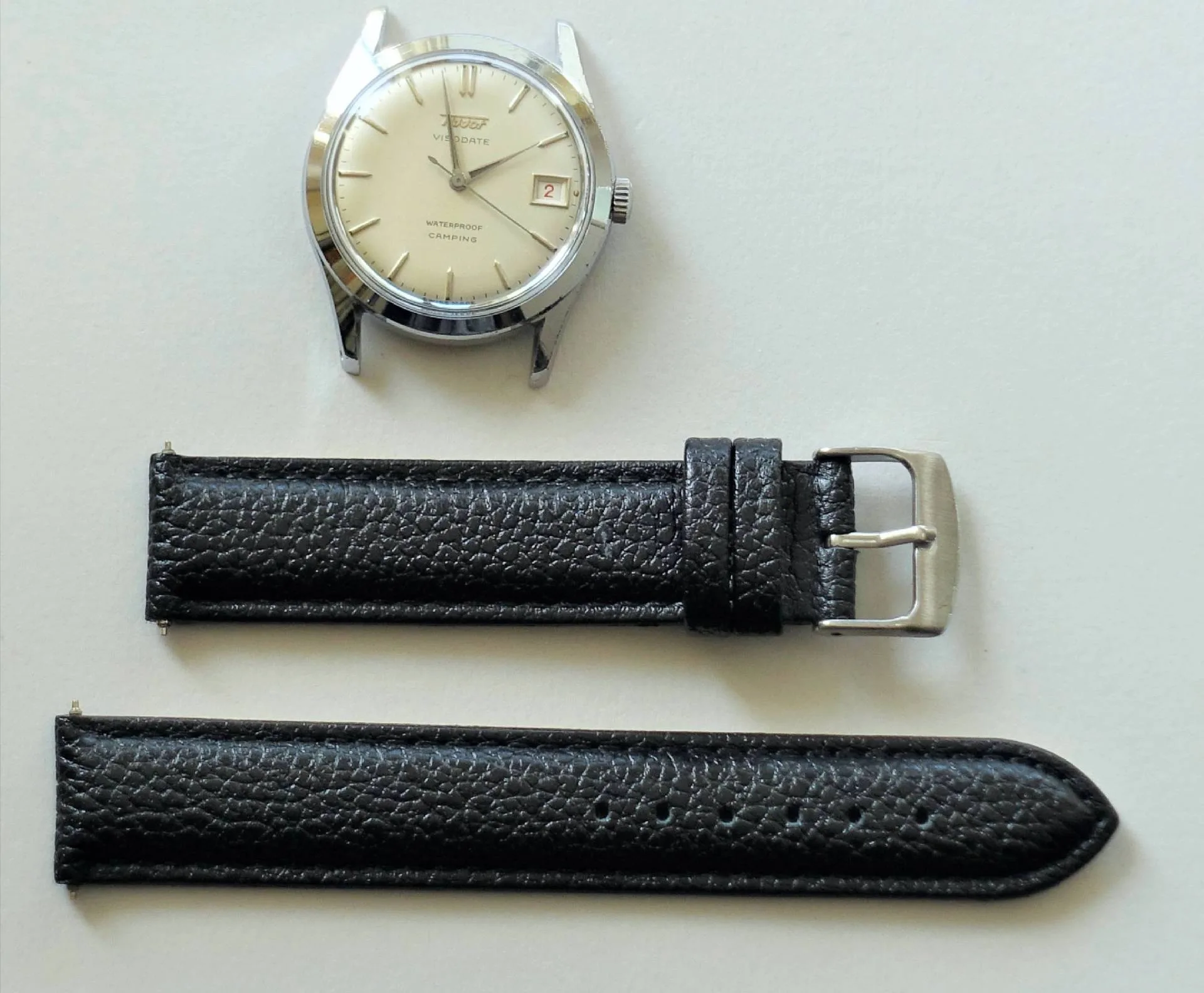 Silberfarbene Armbanduhr mit hellem Zifferblatt und schwarzem Lederarmband in zwei Teilen.