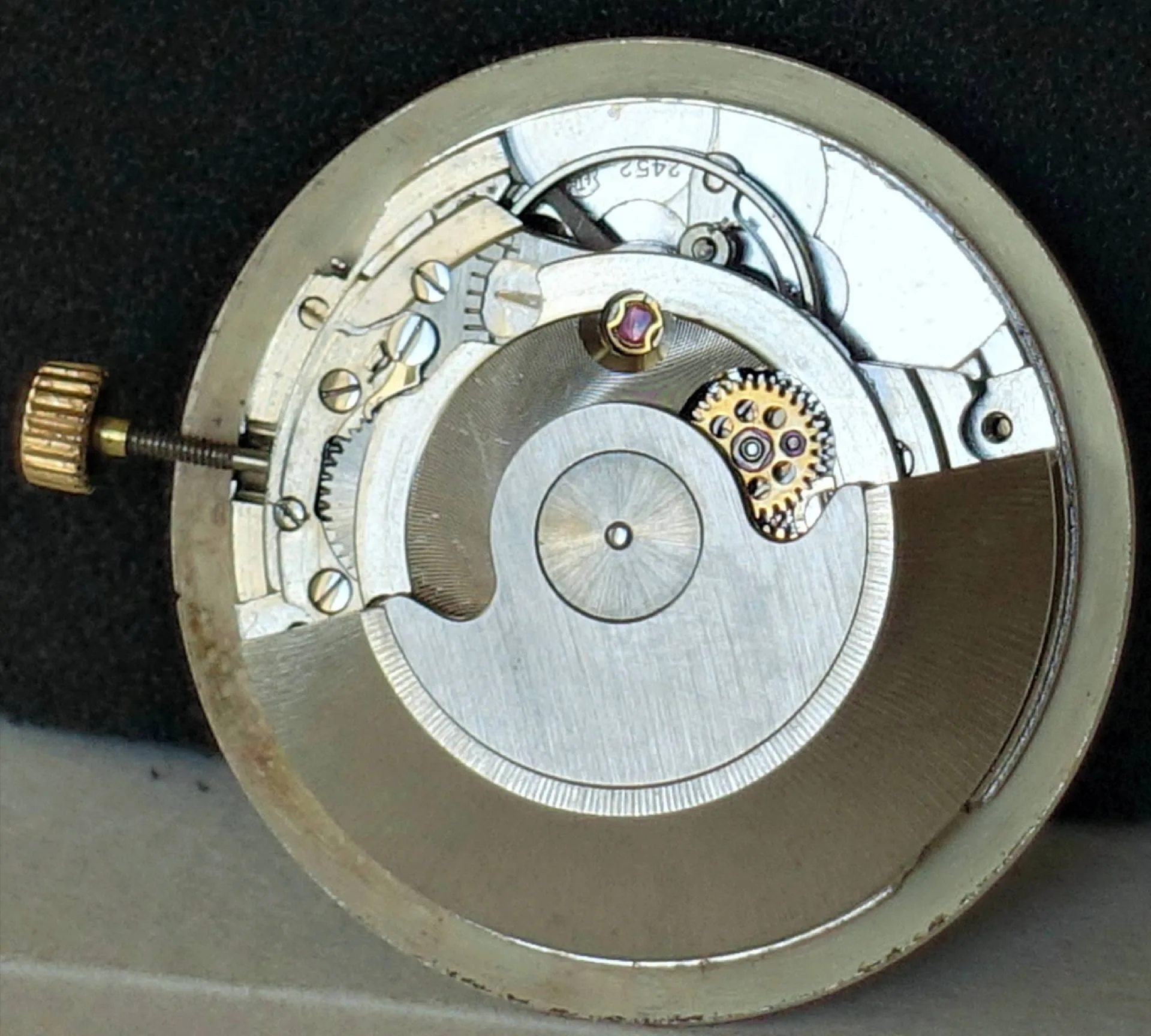 Silberfarbenes Uhrwerk mit goldfarbenen Akzenten Das Bild zeigt ein rundes, silberfarbenes mechanisches Uhrwerk mit sichtbaren Zahnrädern und einer goldfarbenen Aufzugskrone.