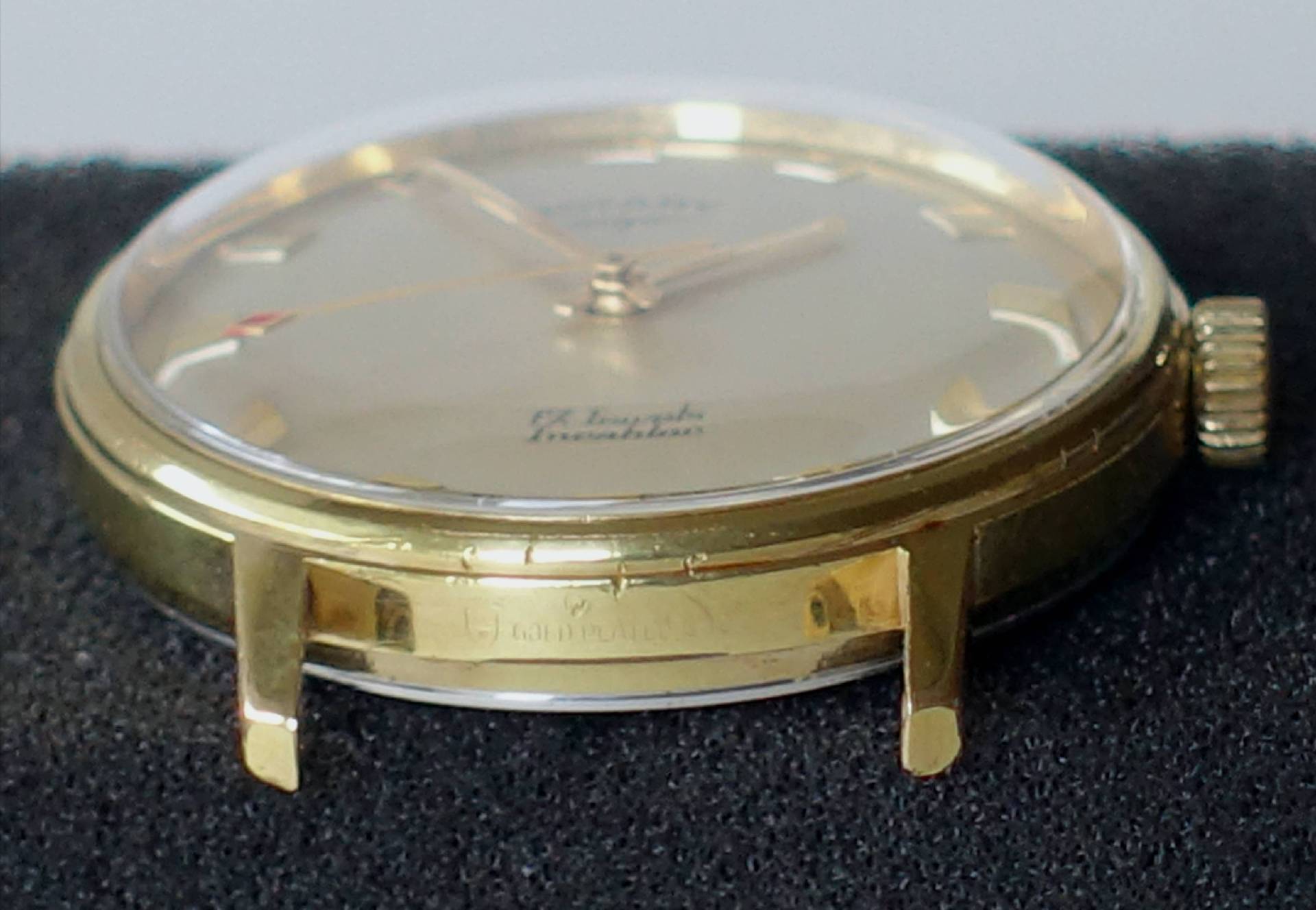 Flache Armbanduhr mit goldfarbenem Gehäuse und hellem Zifferblatt ohne Armband.