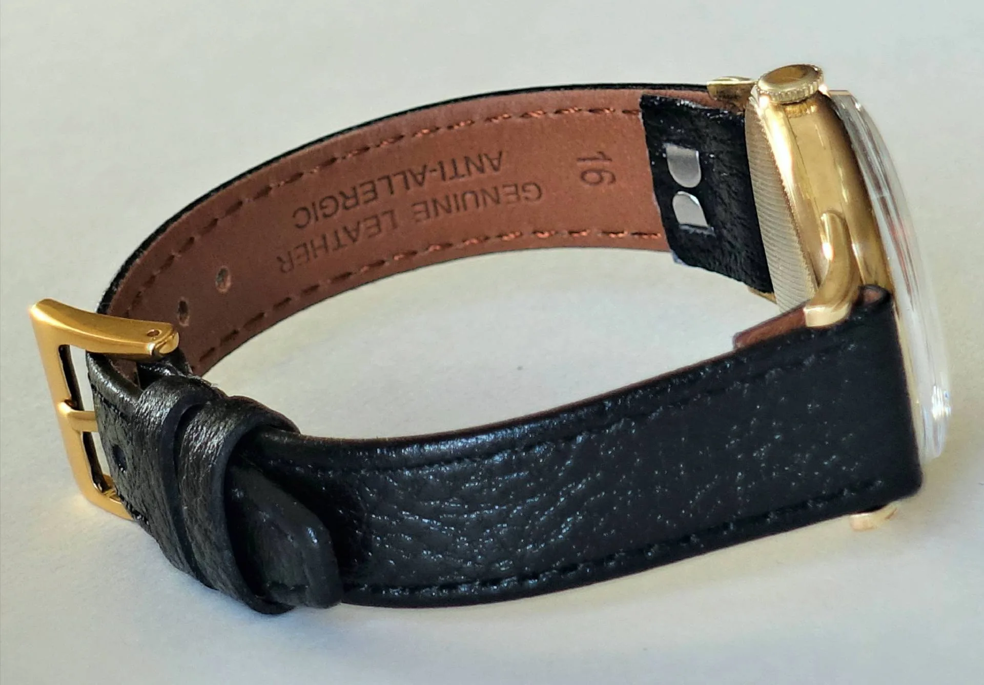 Eine Armbanduhr mit schwarzem Lederband und gelbfarbenem Gehäuse liegt seitlich auf einer hellen Oberfläche.