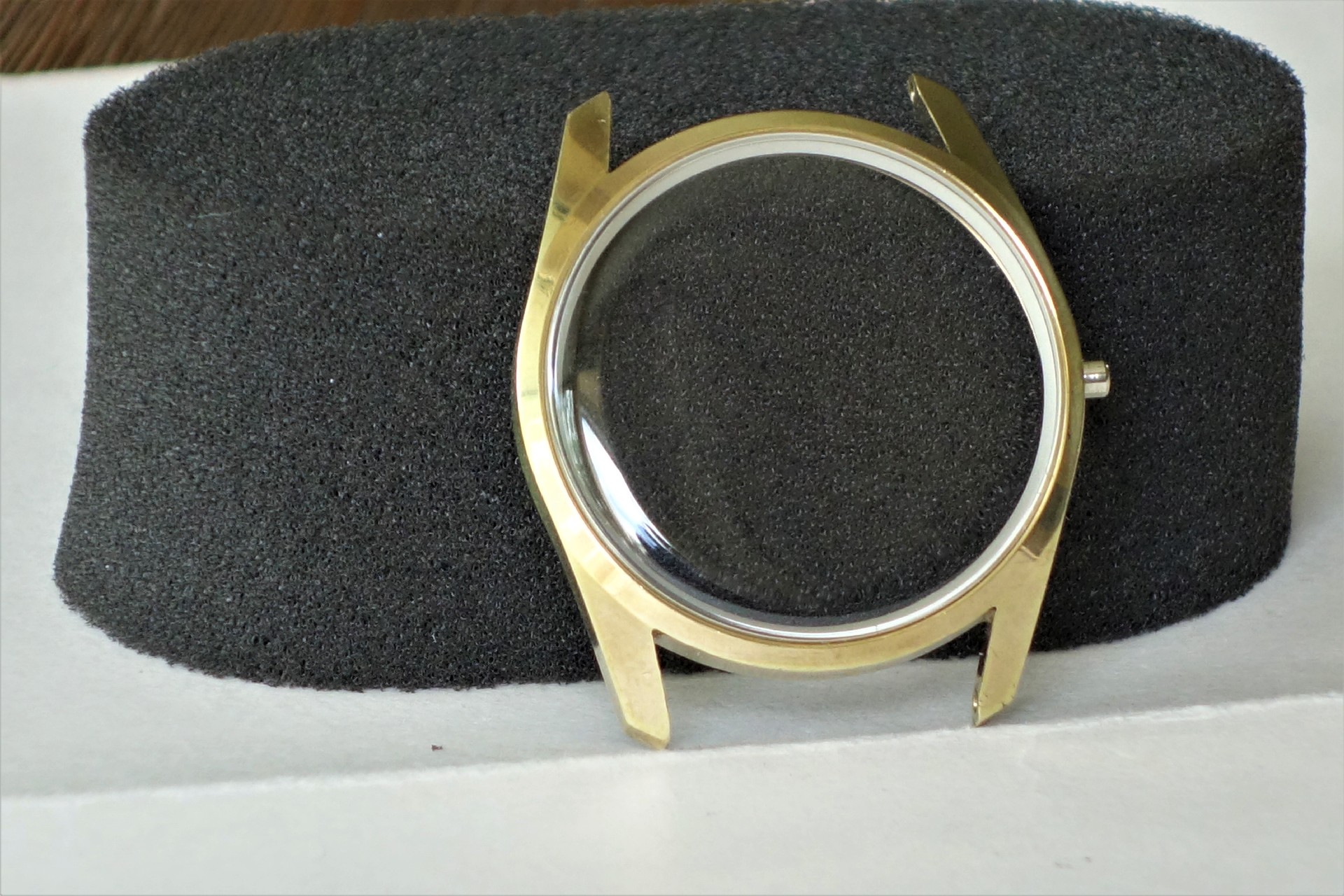 Rundes Uhrgehäuse aus Metall in goldfarbener Optik mit montiertem Uhrglas.